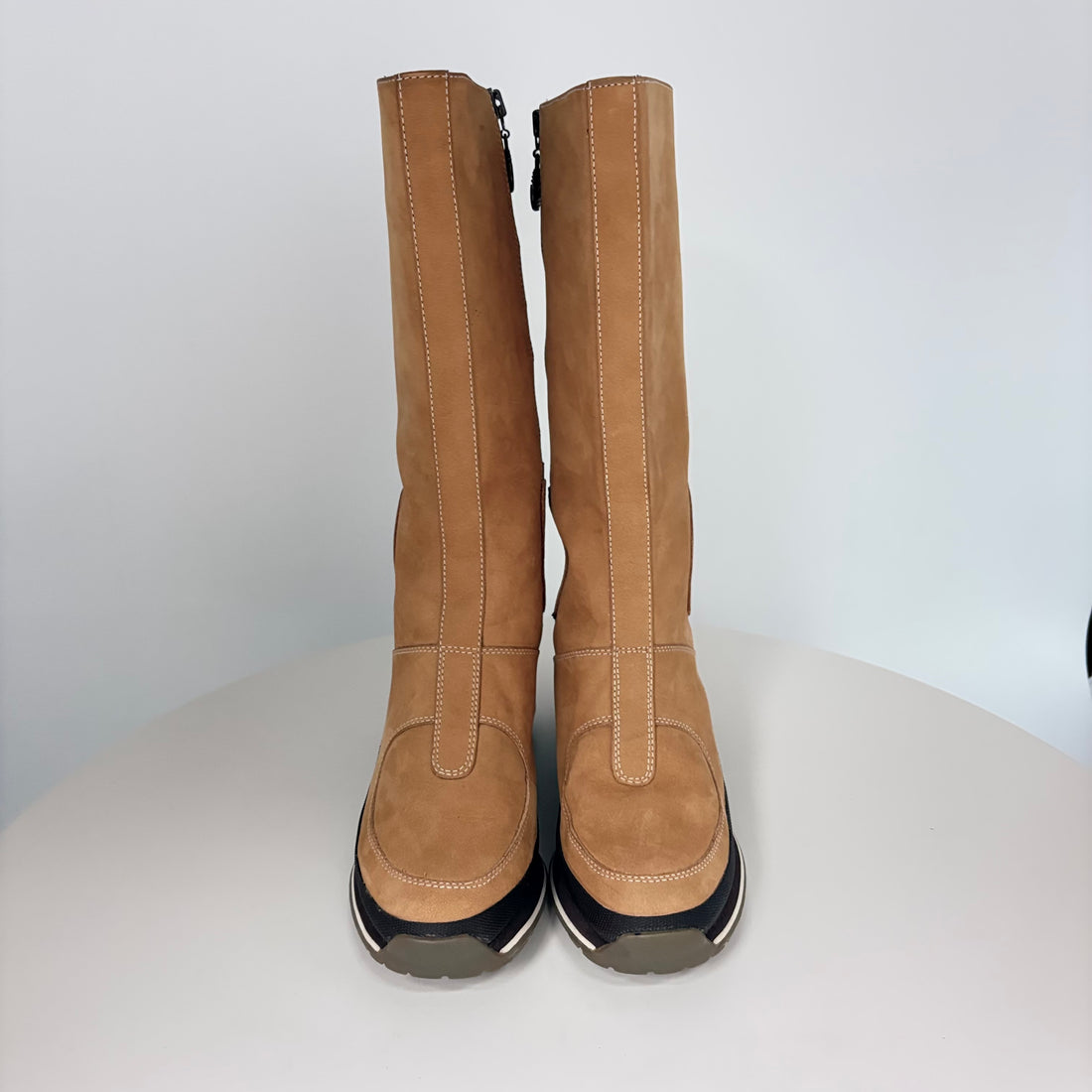 Pair of tan knee-high boots with black soles on a white background