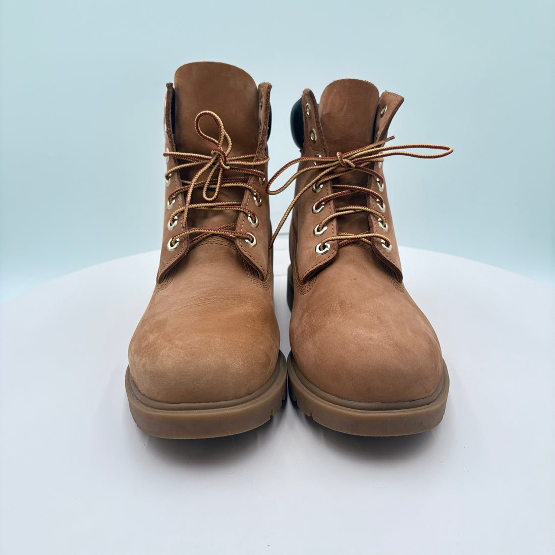Pair of brown leather boots on a white platform with a light blue background