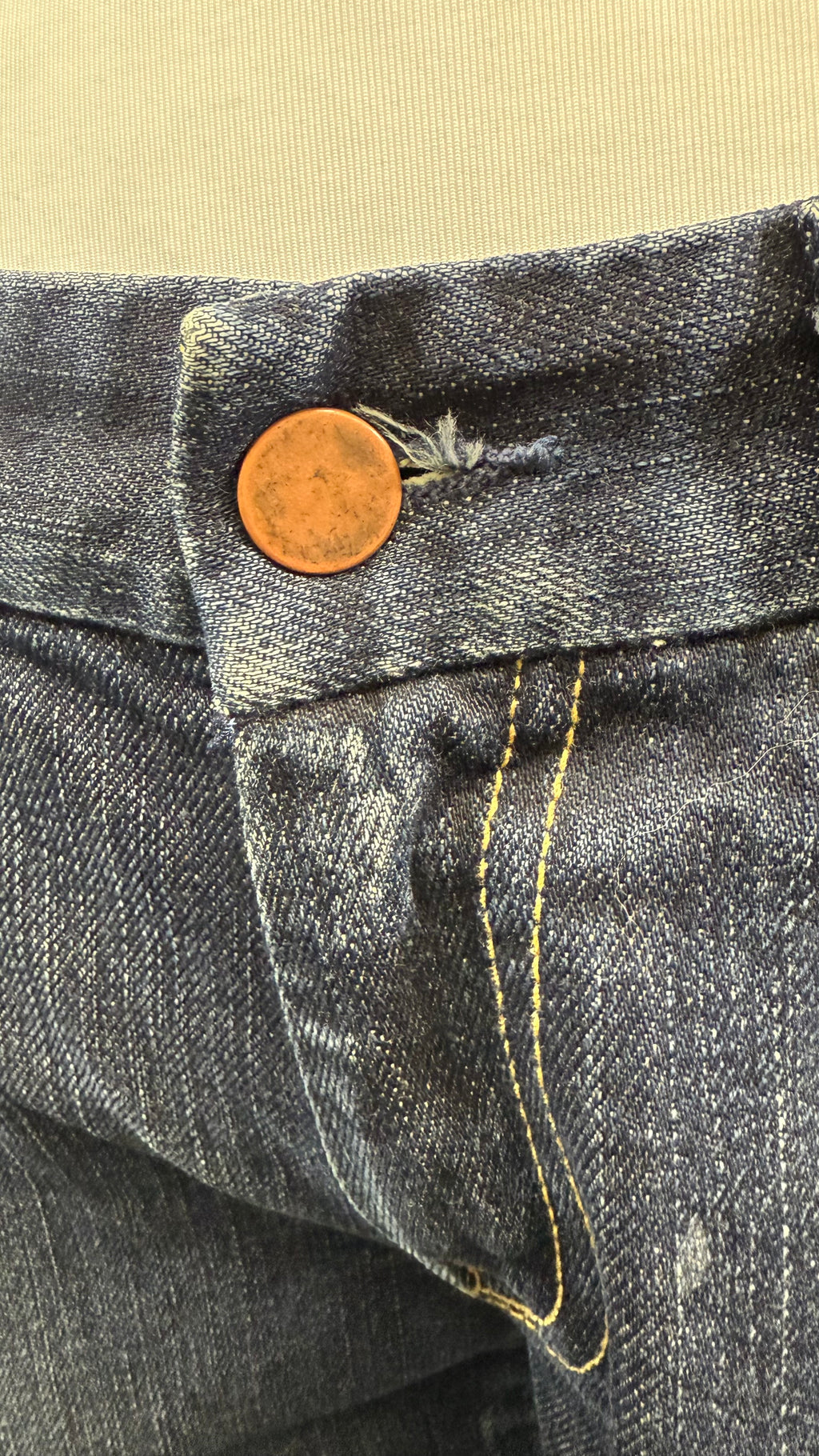 Close-up of a button on a pair of jeans with a beige background