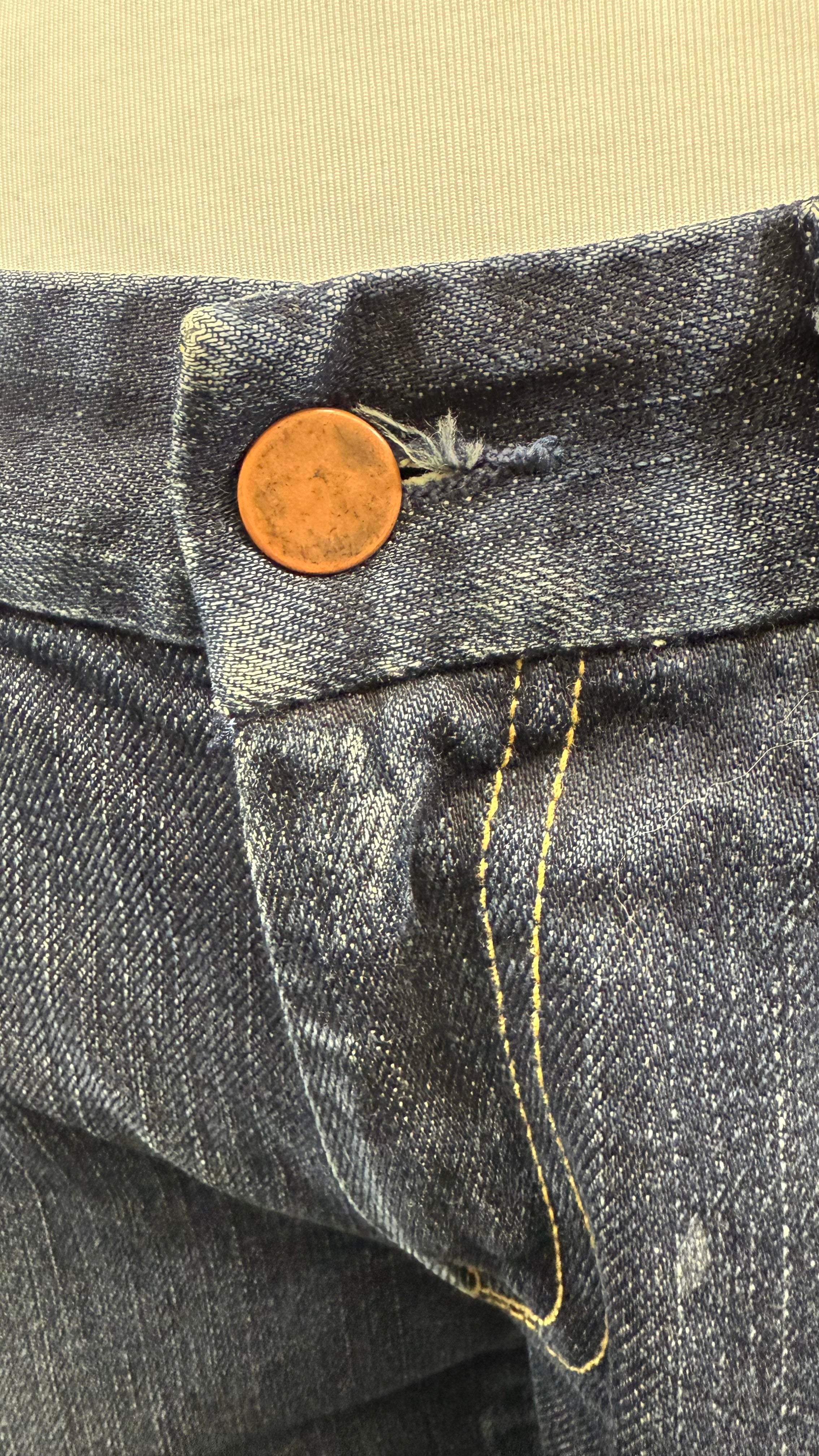 Close-up of a button on a pair of jeans with a beige background