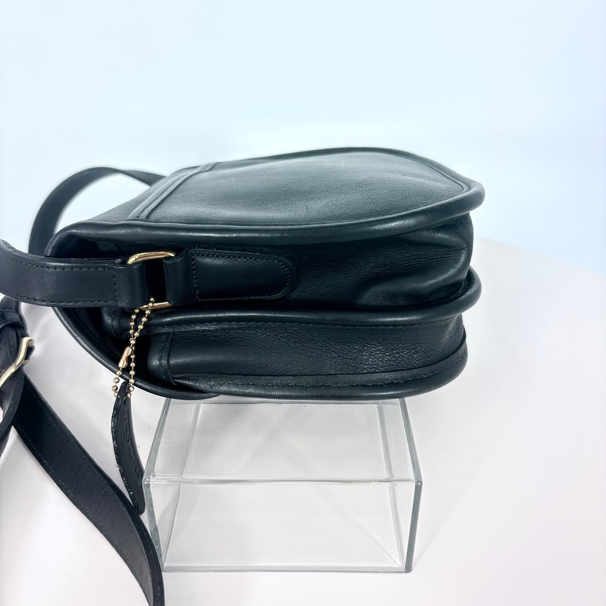 Black leather handbag on a clear stand against a light gray background