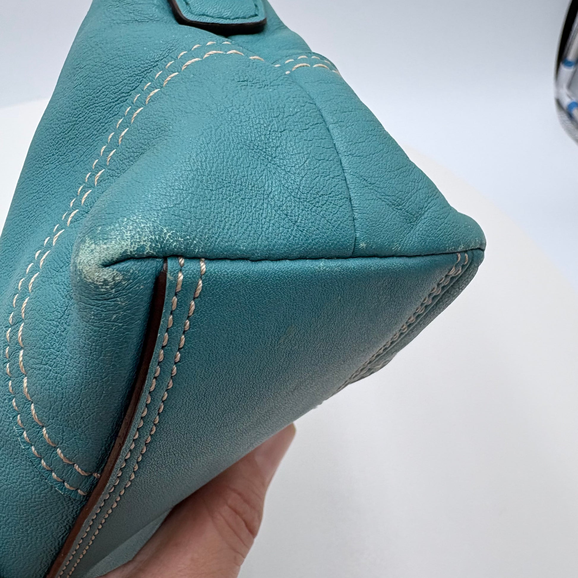 Teal leather bag with visible wear and tear on a white background