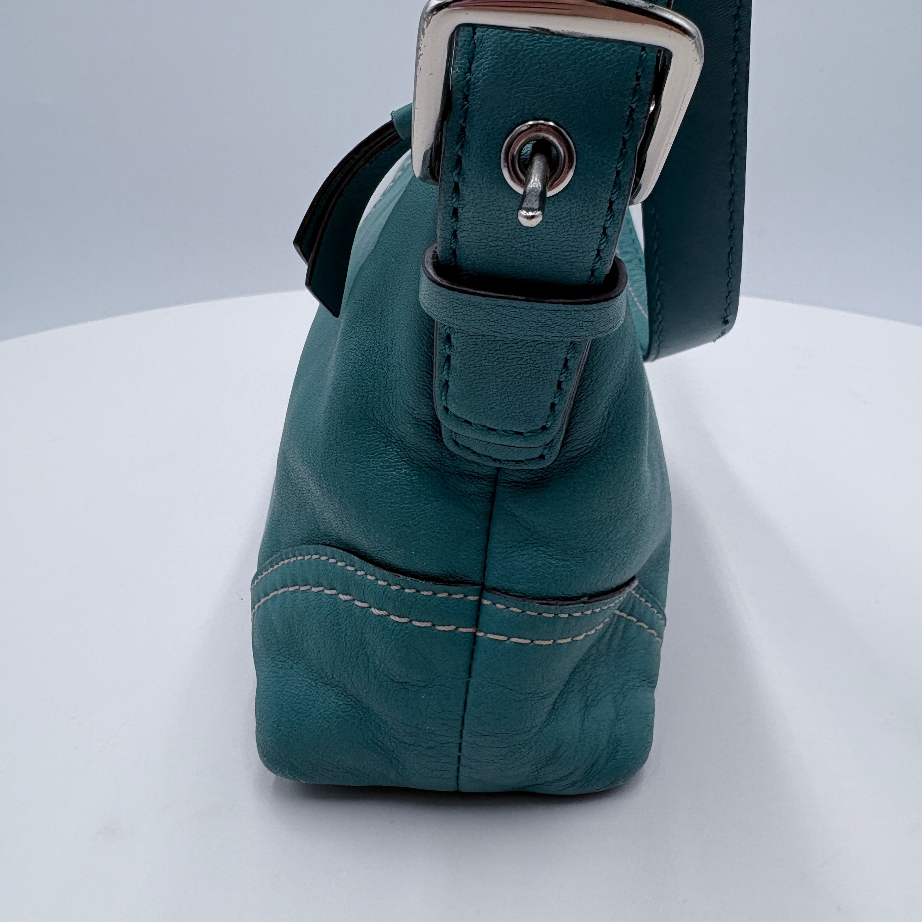 Teal leather bag with a silver buckle on a white background
