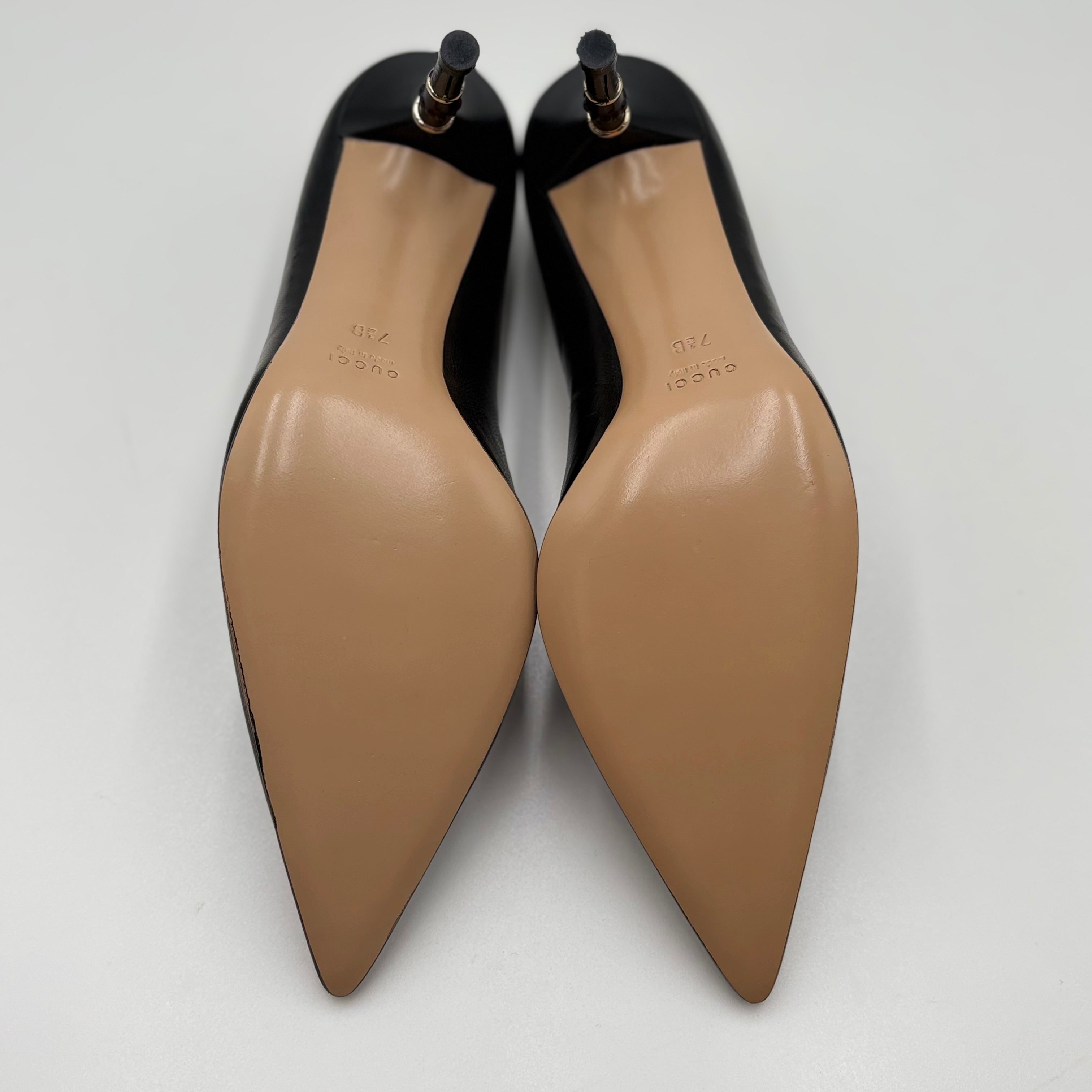 Pair of black high-heeled shoes with tan soles on a white background