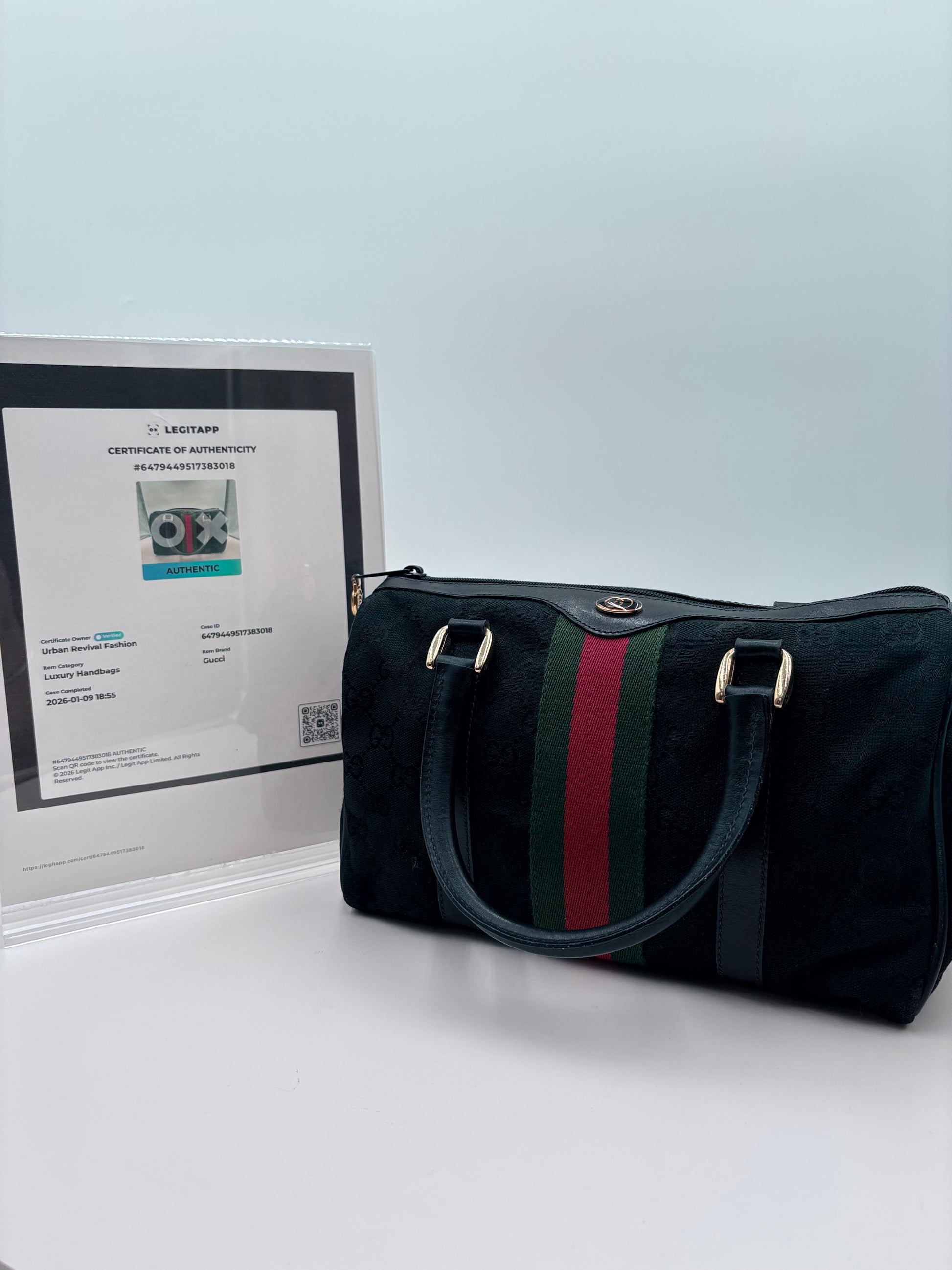 Black handbag with green and red stripe on a light gray surface