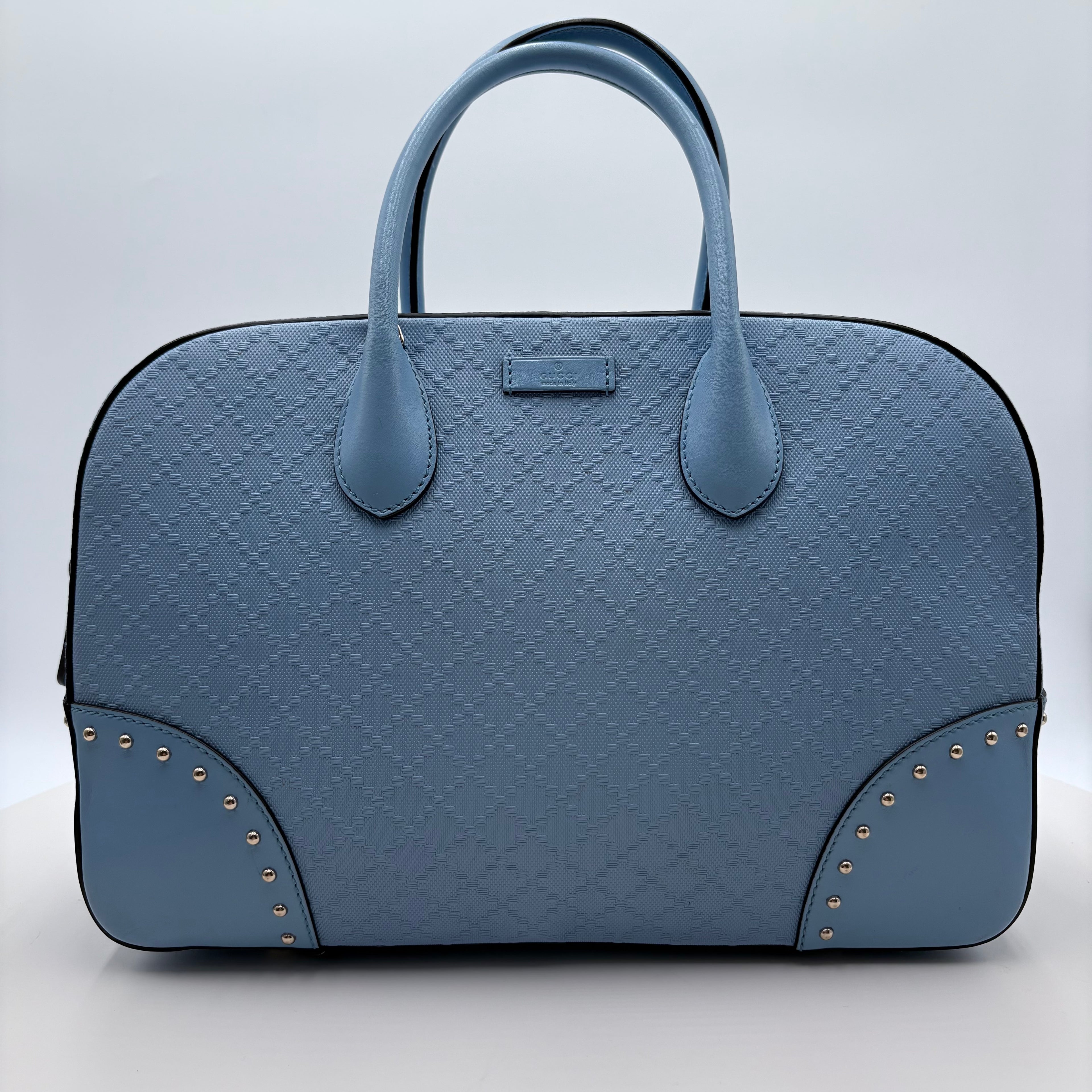 Blue textured handbag with gold studs on a light gray background