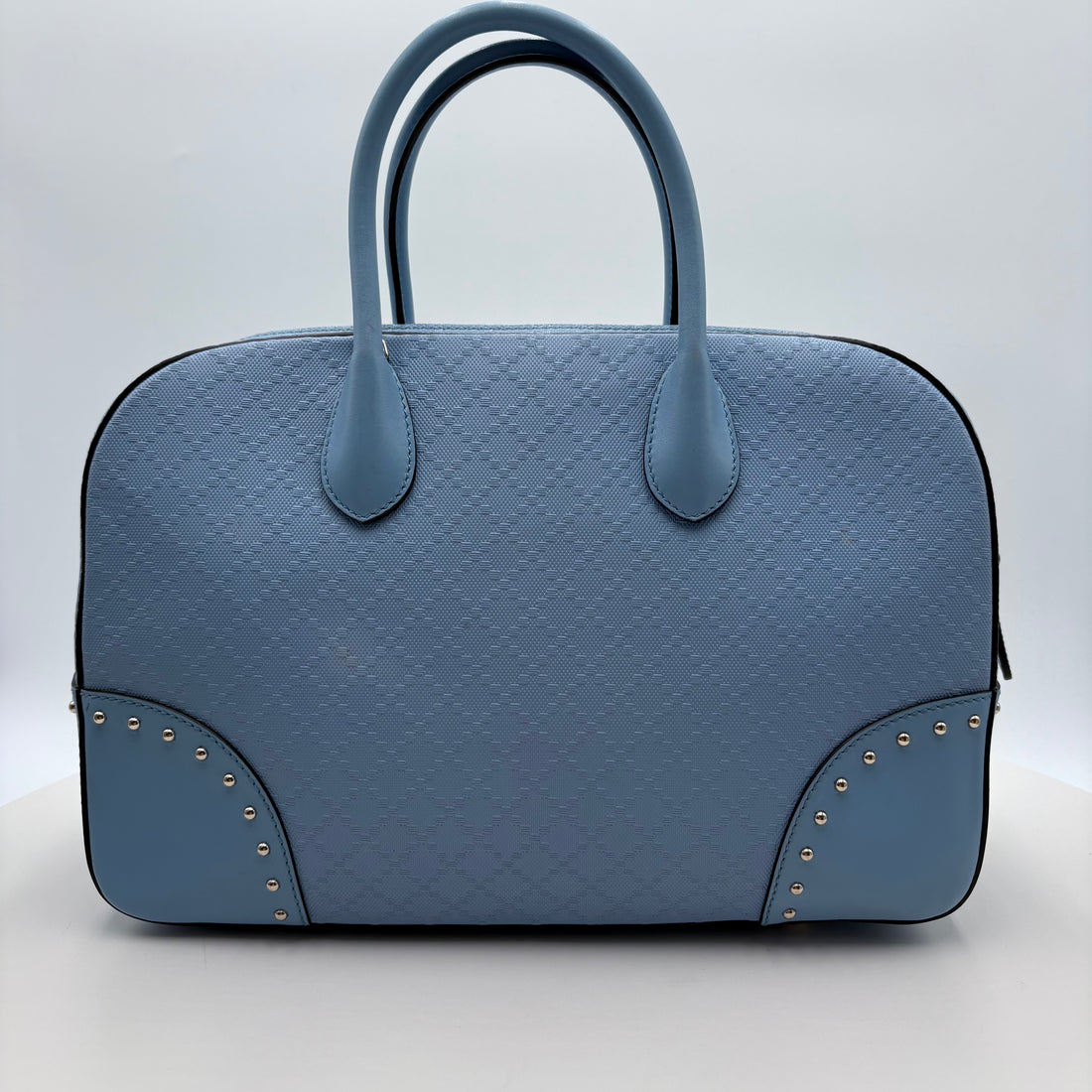 Blue textured Gucci handbag with studded details on a light gray background