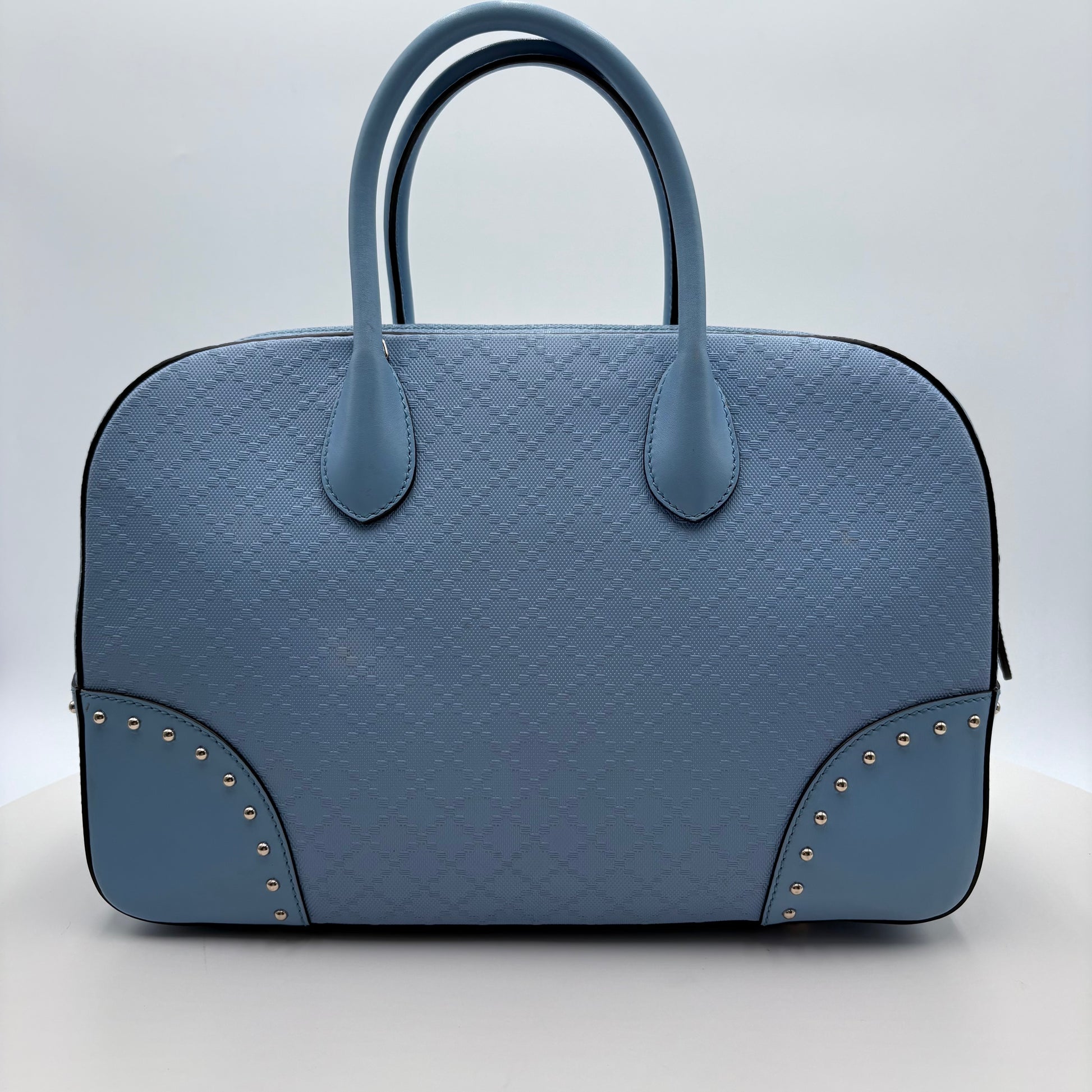 Blue textured Gucci handbag with studded details on a light gray background