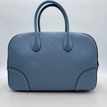Blue textured Gucci handbag with studded details on a light gray background