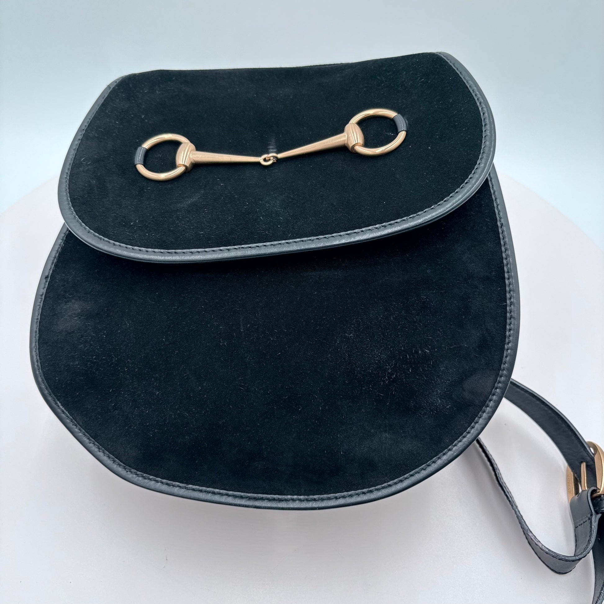 Black leather bag with gold equestrian buckle on a light gray background