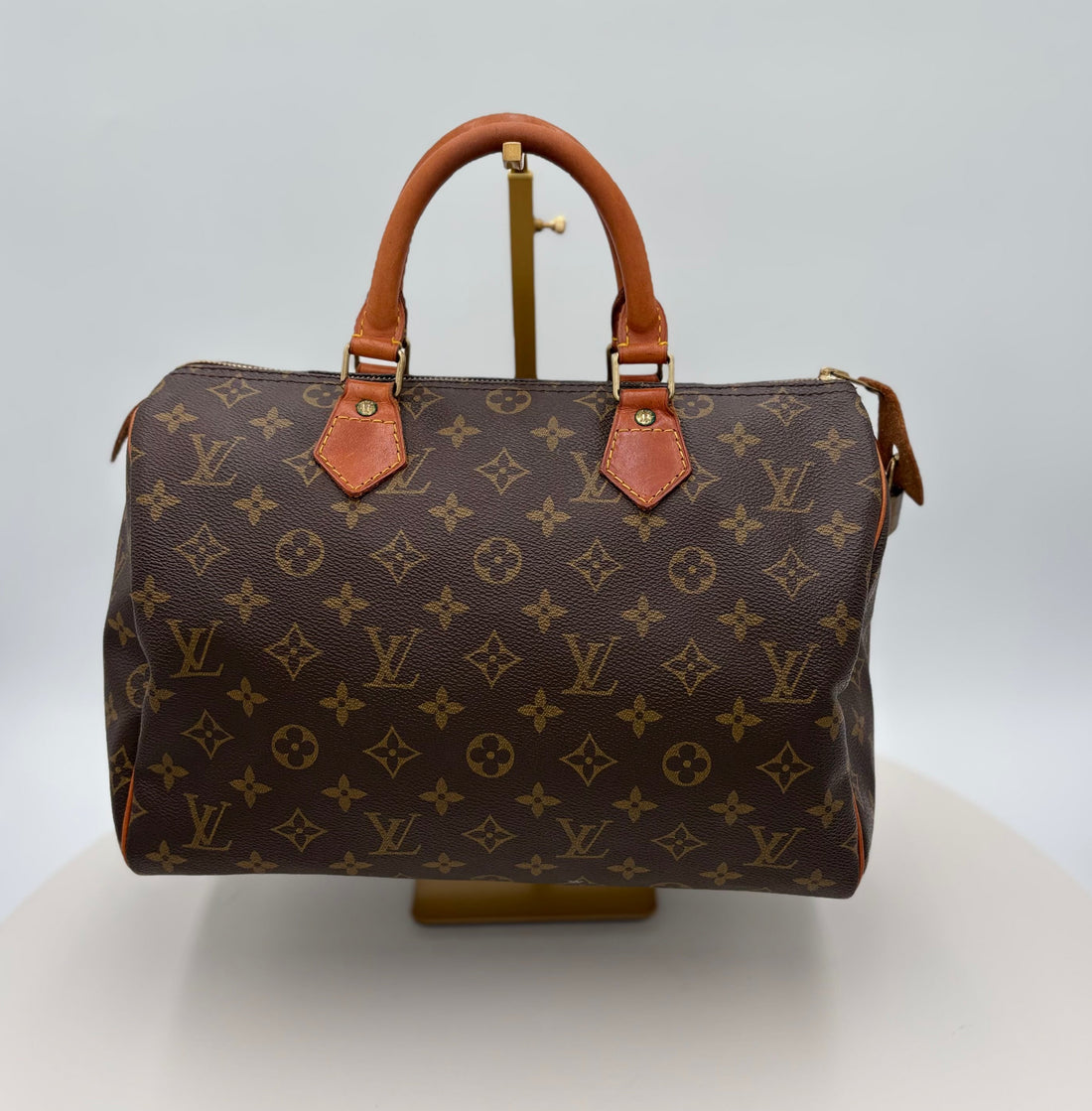 Brown Louis Vuitton handbag with monogram pattern on a white stand against a light gray background