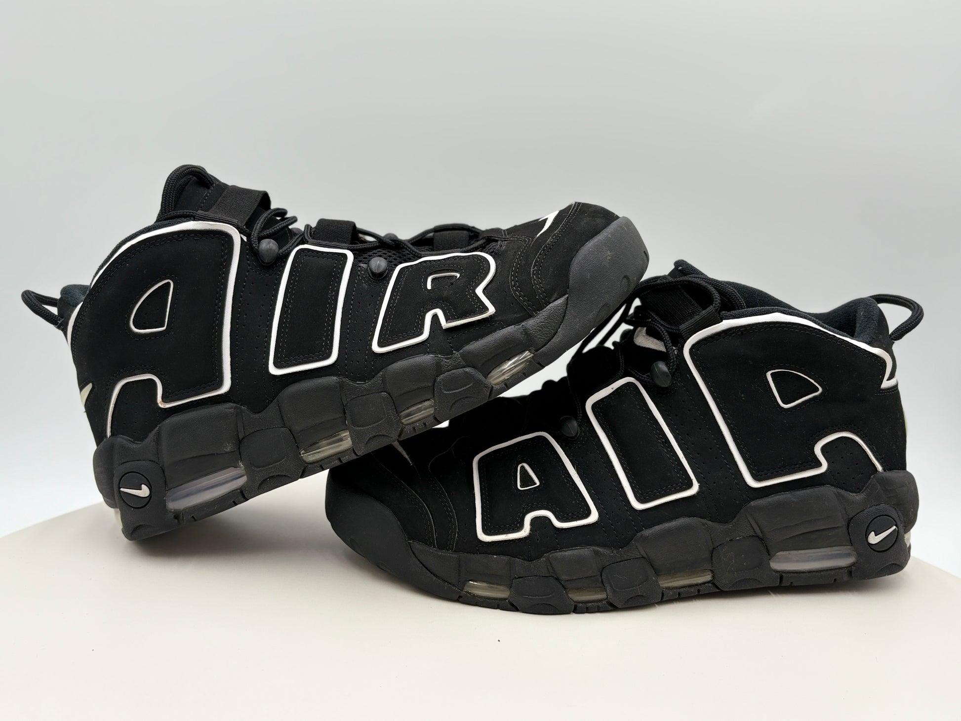 Black Nike Air More Uptempo sneakers with white accents on a light gray background