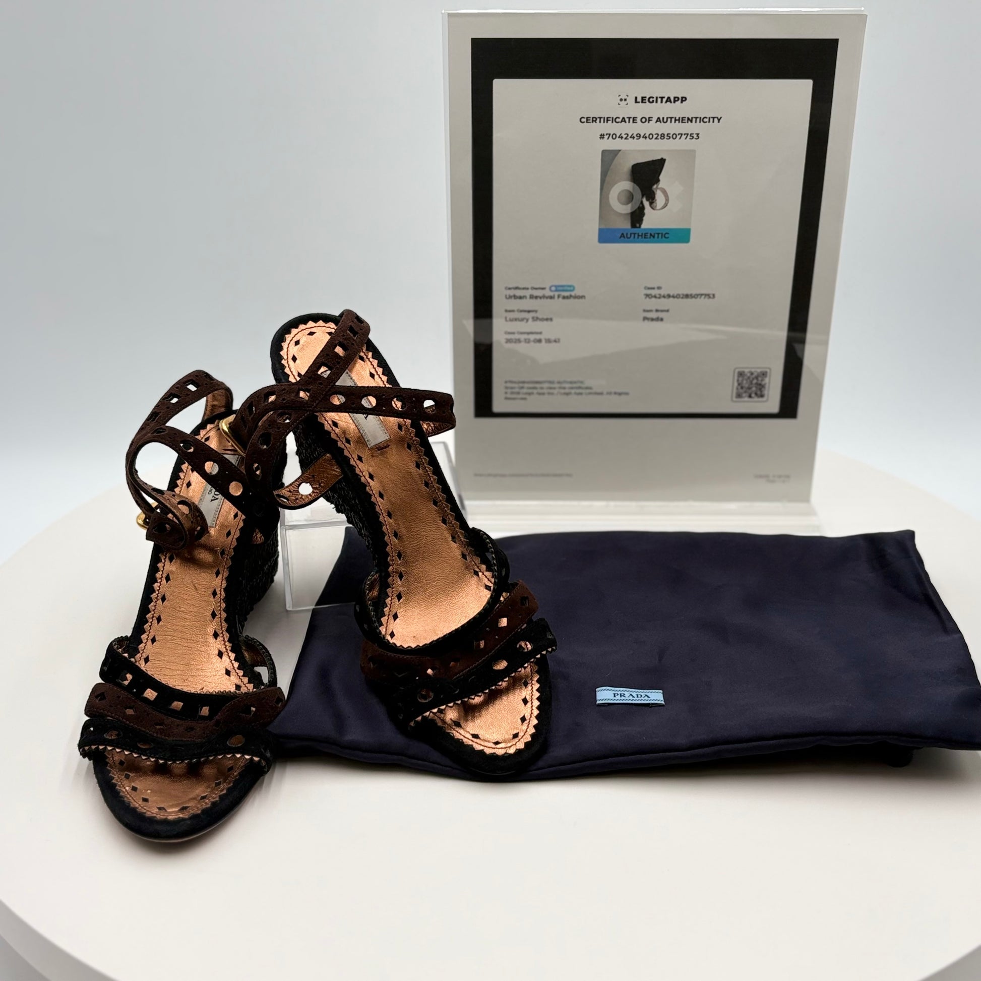 Pair of black strappy sandals with a Prada dust bag and certificate of authenticity on a white background