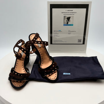 Pair of black strappy sandals with a Prada dust bag and certificate of authenticity on a white background