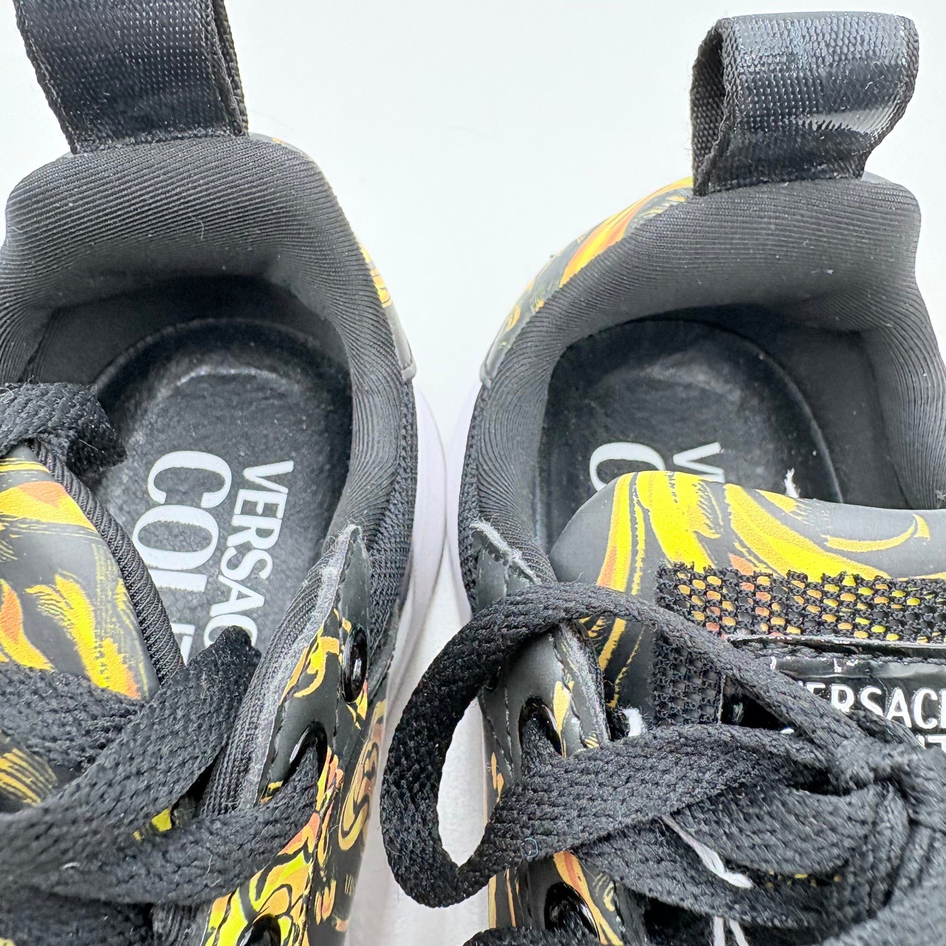 Black and yellow Versace shoes with floral patterns on a white background