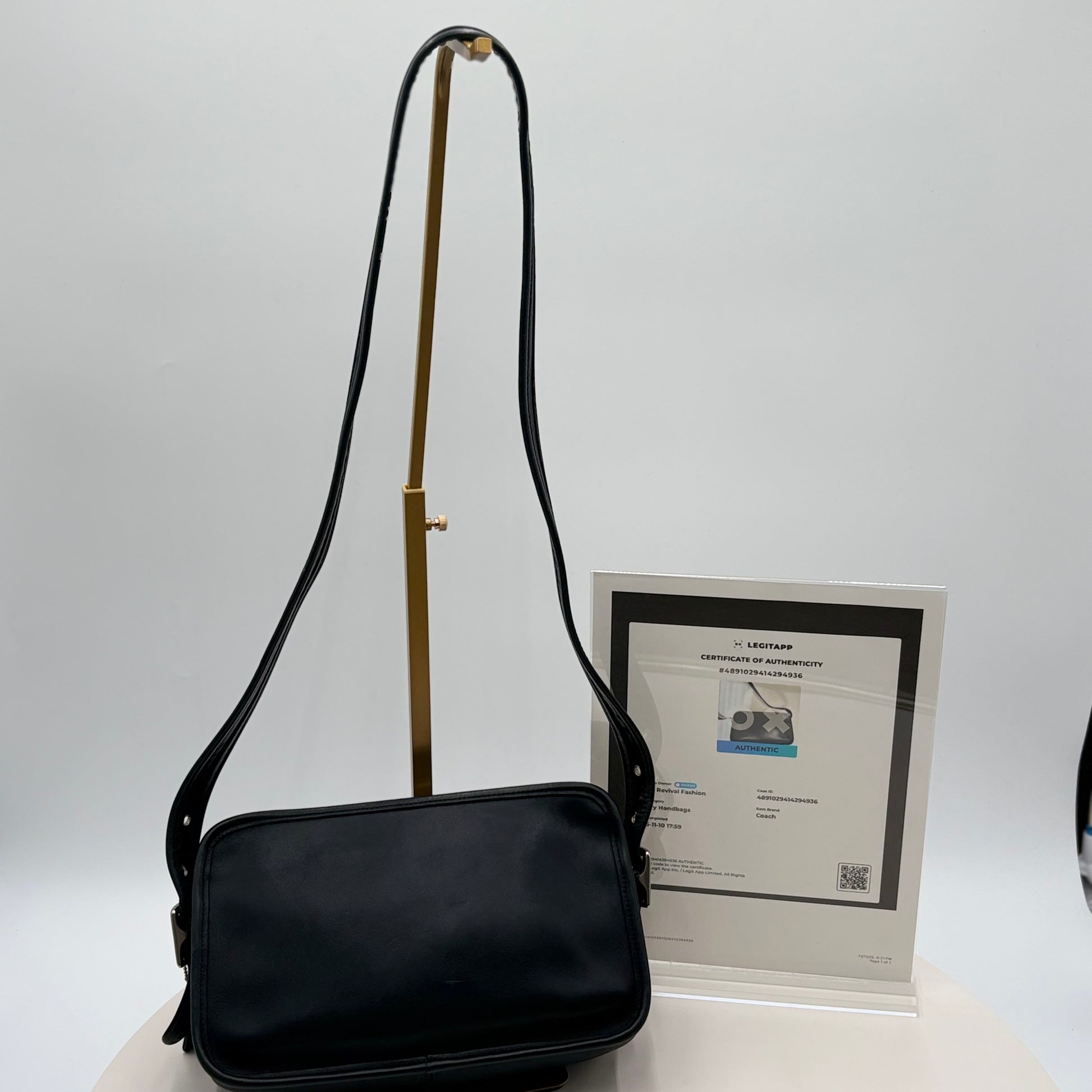 Black shoulder bag on a white background with a certificate of authenticity in the background.