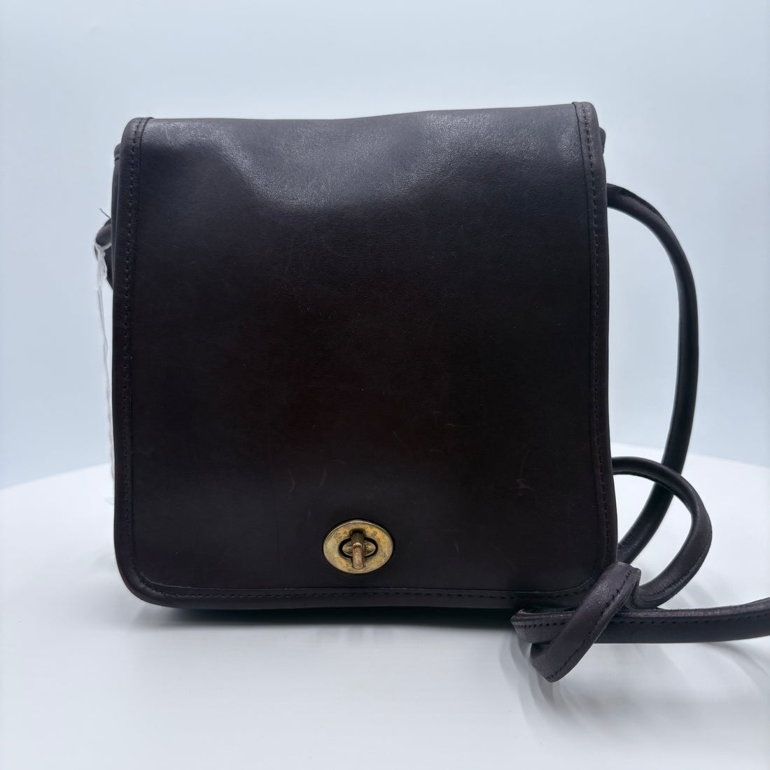 Black leather crossbody bag with a gold clasp on a light gray background