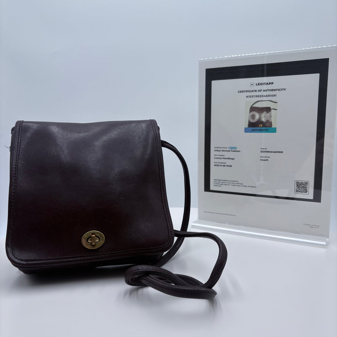 Black leather crossbody bag with a gold clasp on a light gray background