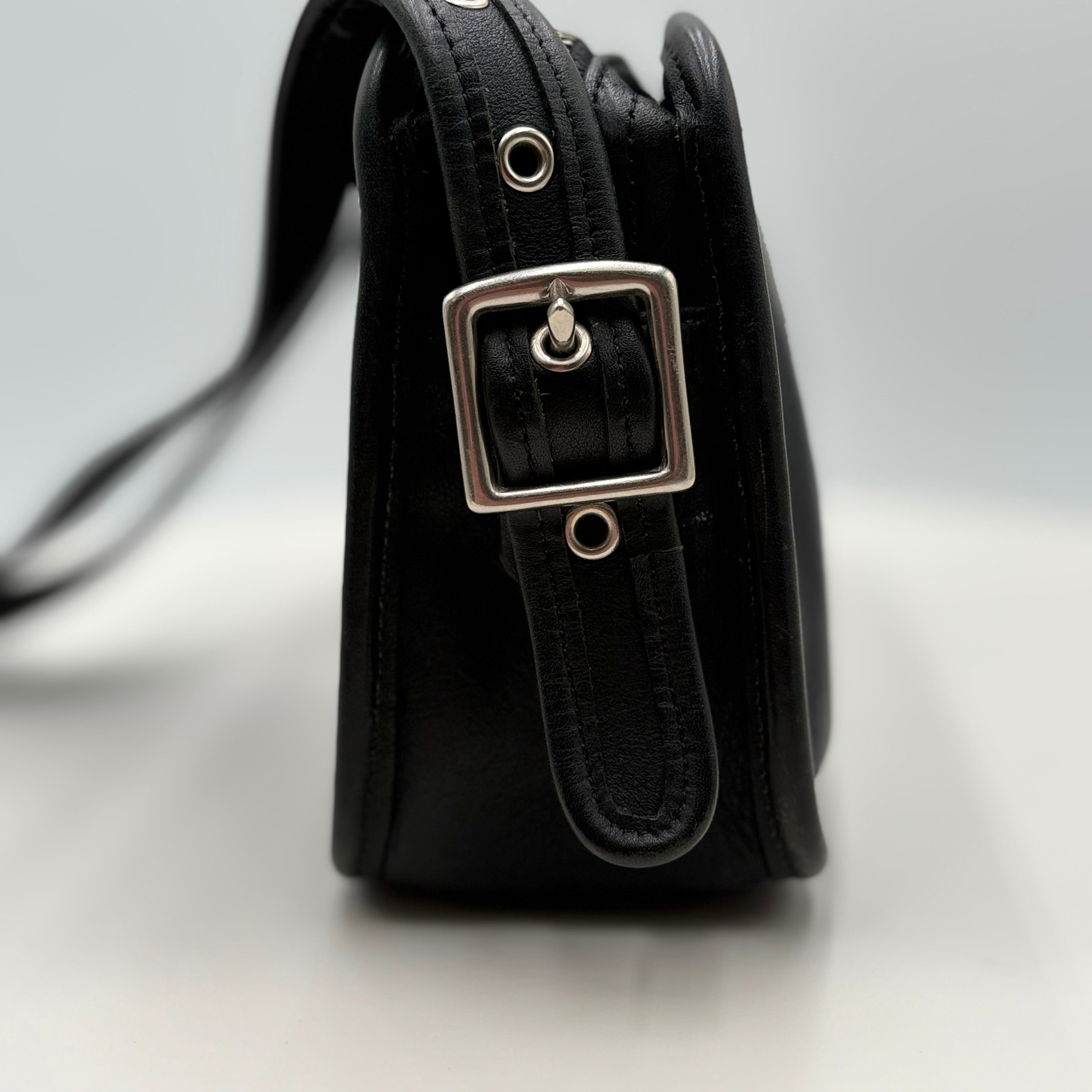 Black leather handbag with silver buckle on a light gray background