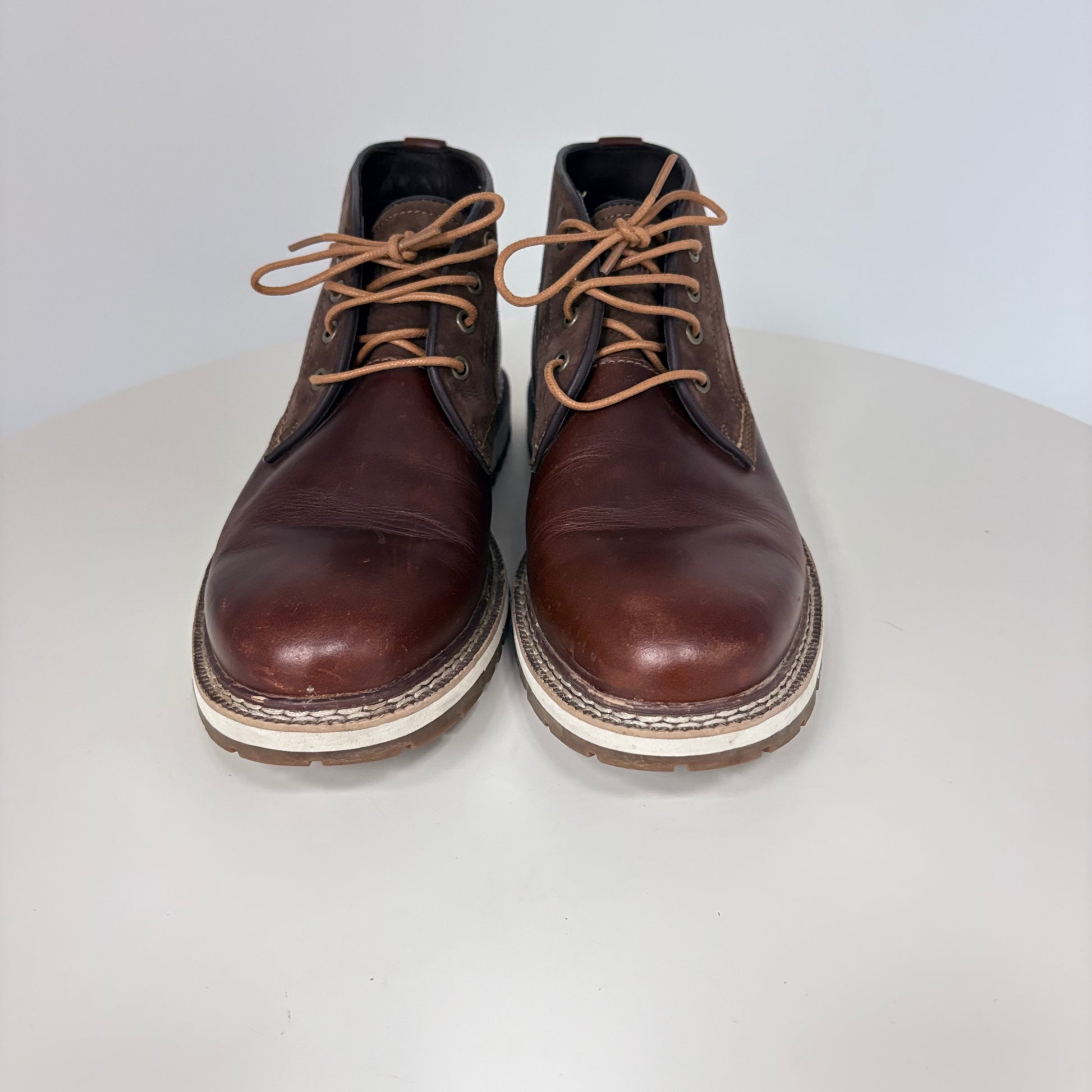 Pair of brown leather boots with white soles on a light gray background