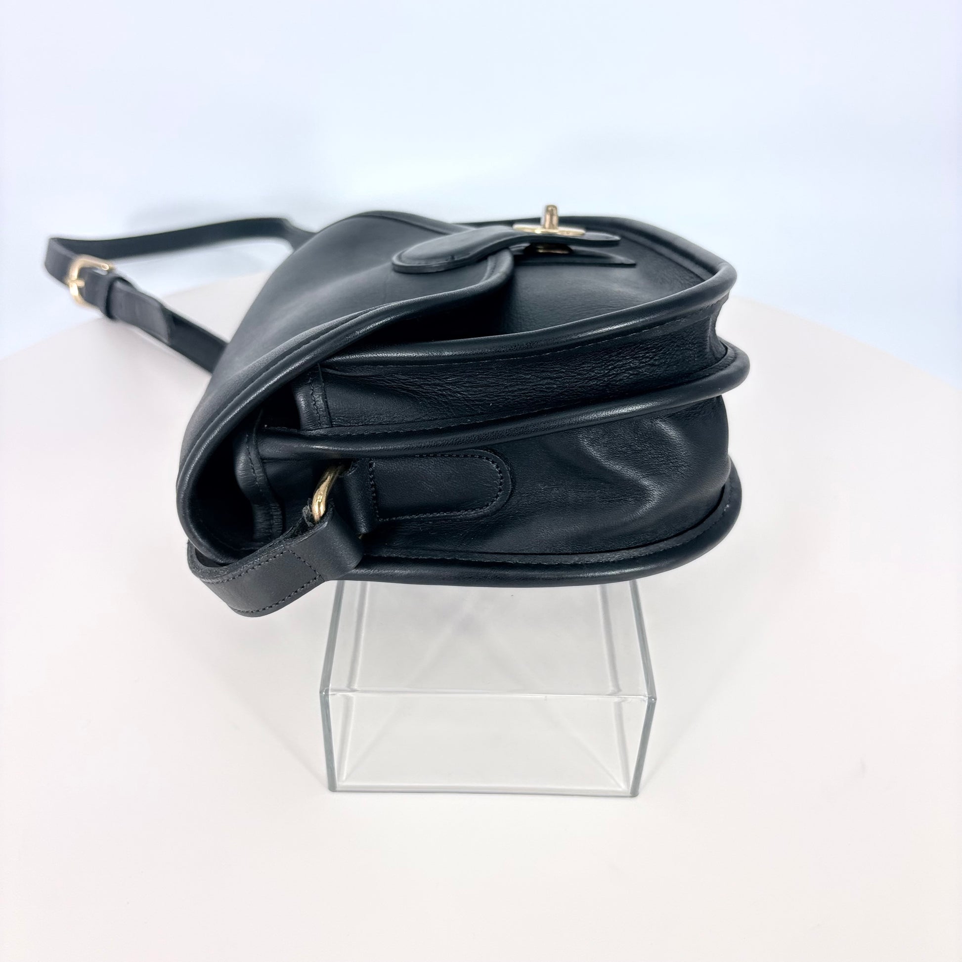 Black leather handbag on a clear stand against a white background