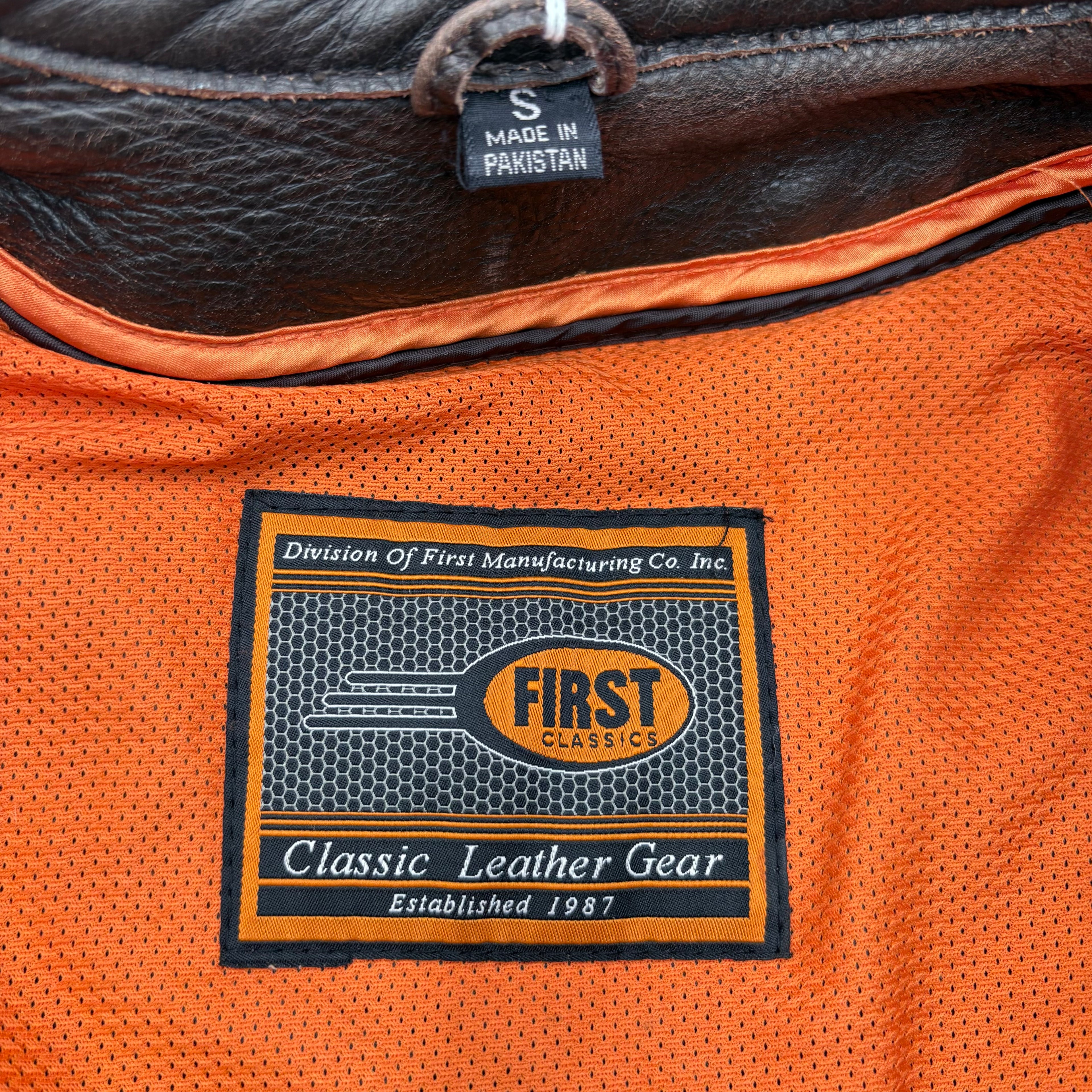 Close-up of a leather bag with a 'First Classics' label on an orange background.