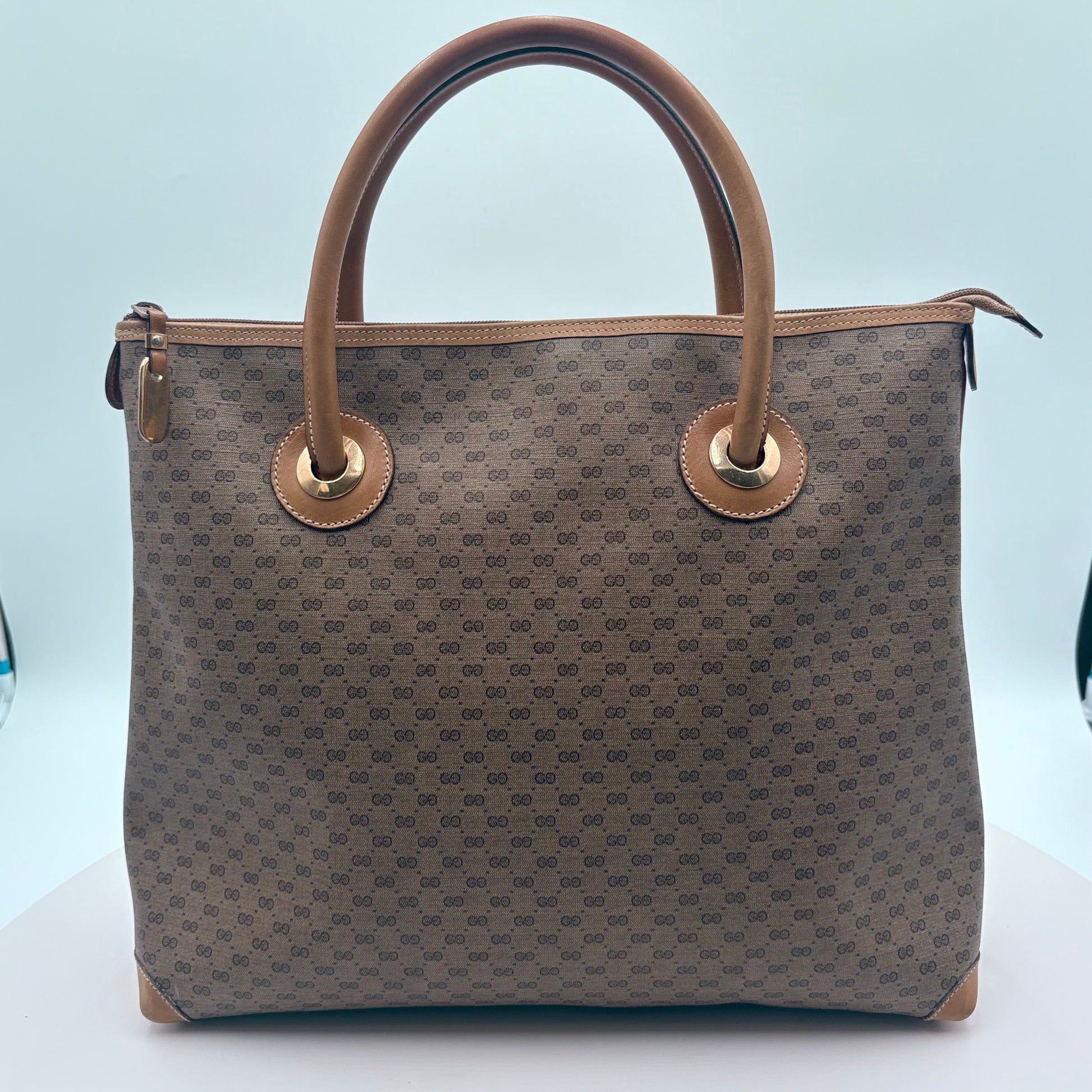 Brown patterned handbag with tan handles on a light blue background