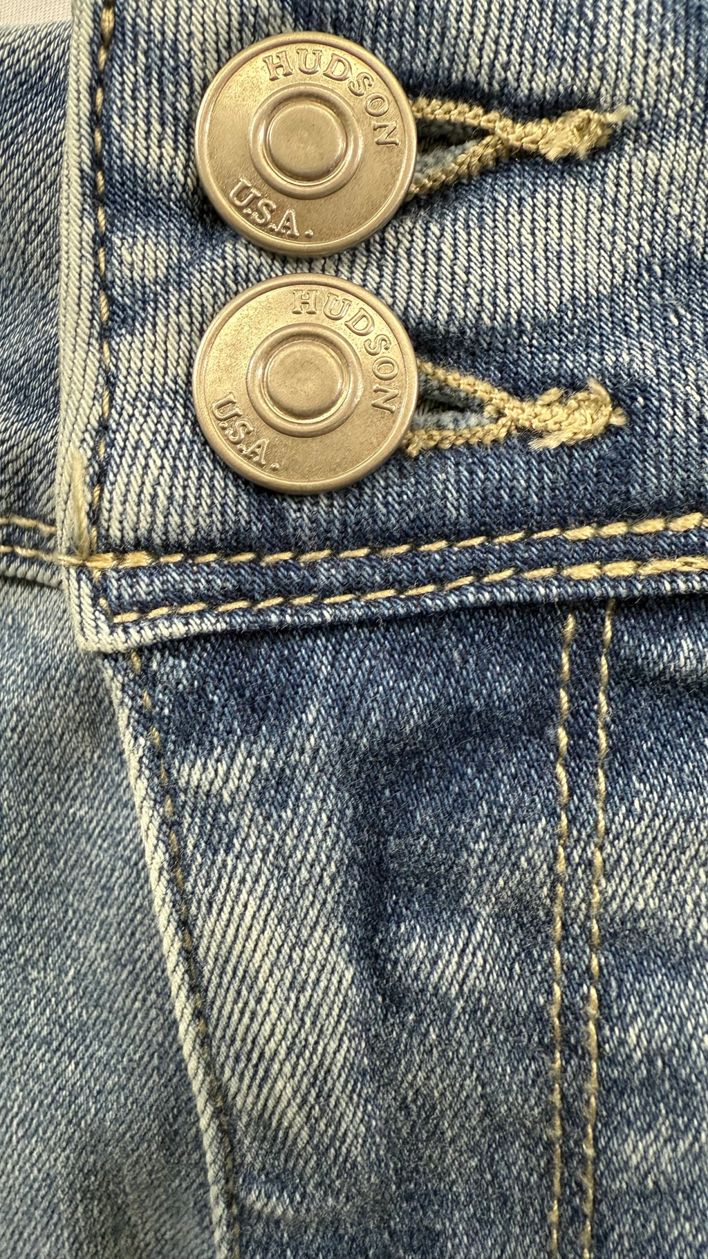 Close-up of a pair of blue jeans with gold buttons and 'Hudson' branding.