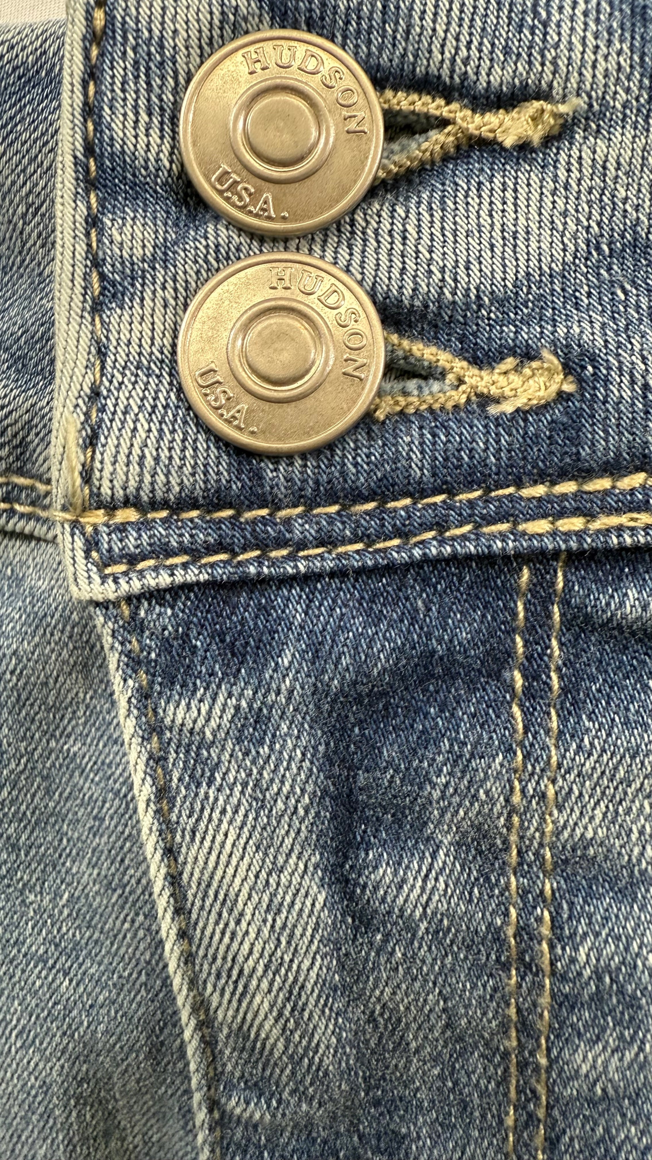 Close-up of a pair of blue jeans with gold buttons and 'Hudson' branding.
