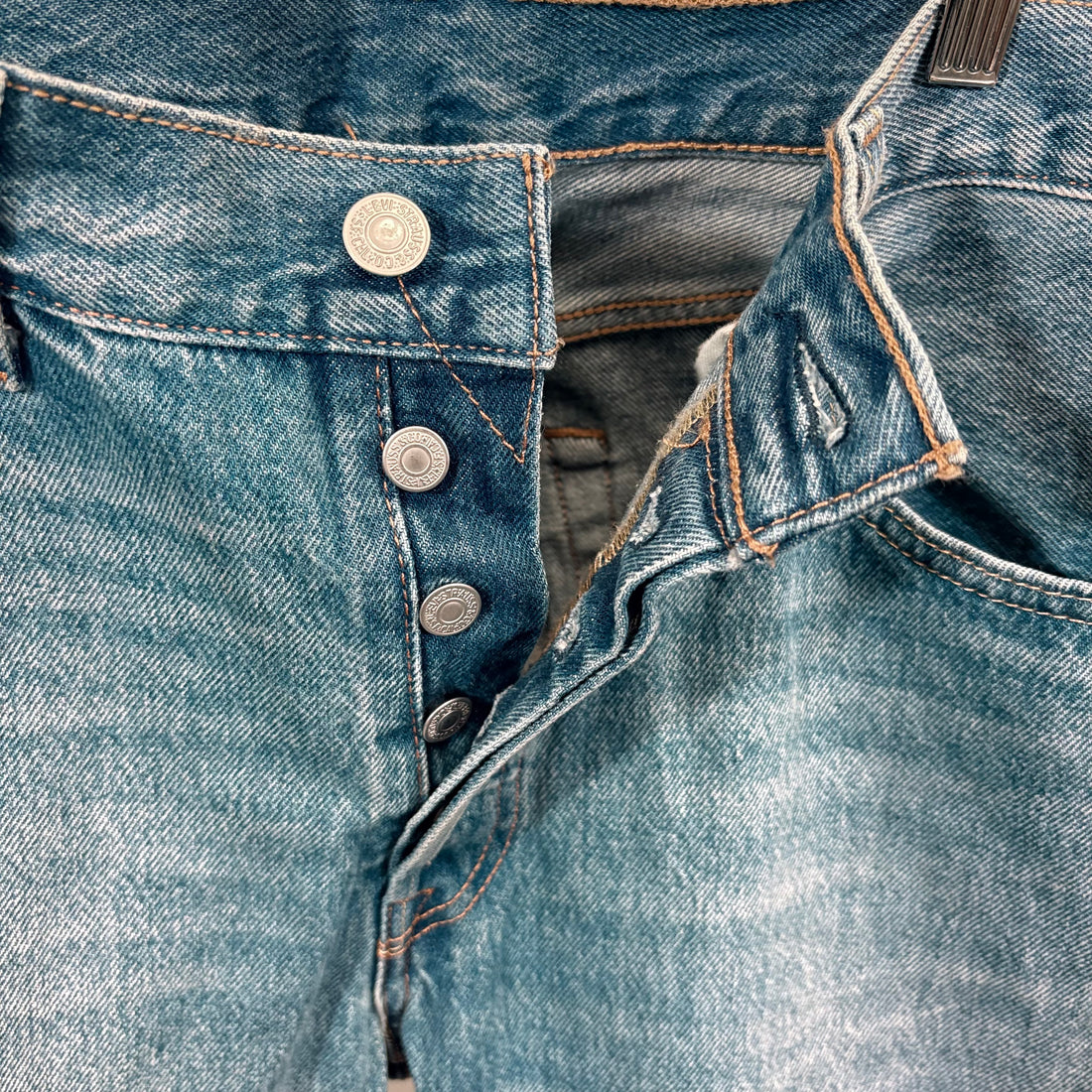 Close-up of blue denim jeans with buttons and stitching details.