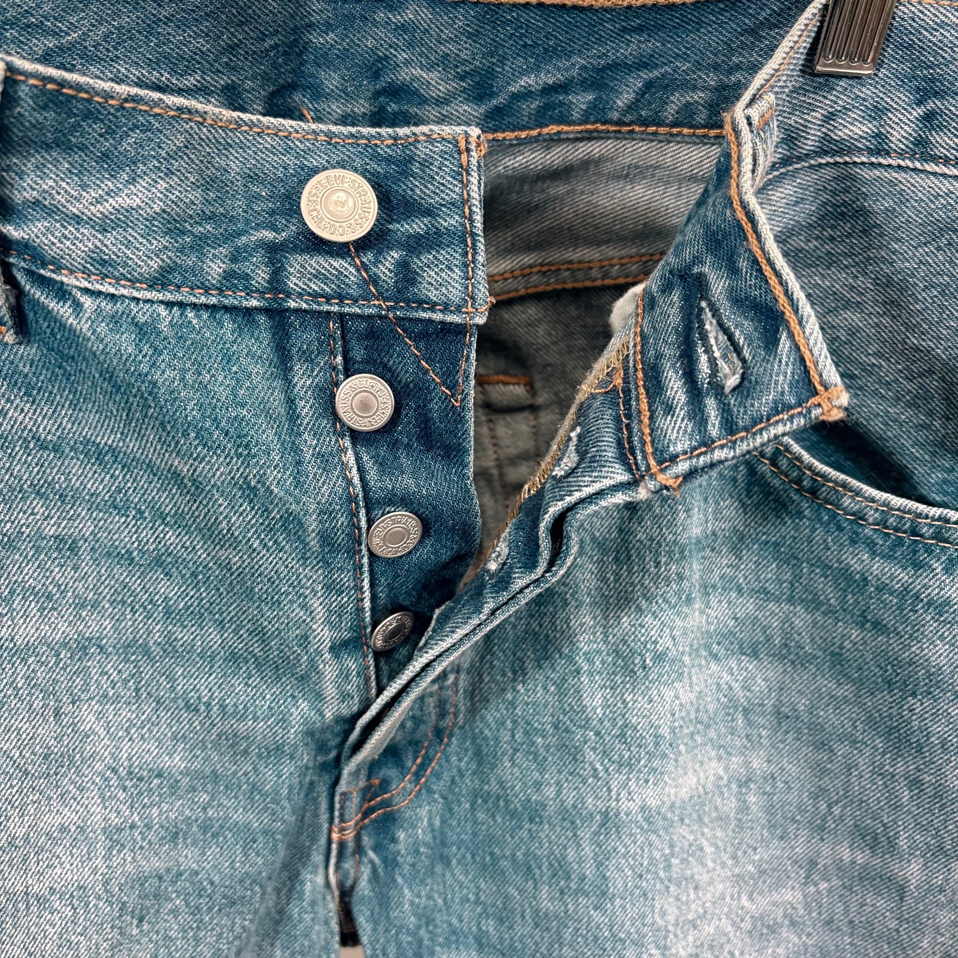 Close-up of blue denim jeans with buttons and stitching details.