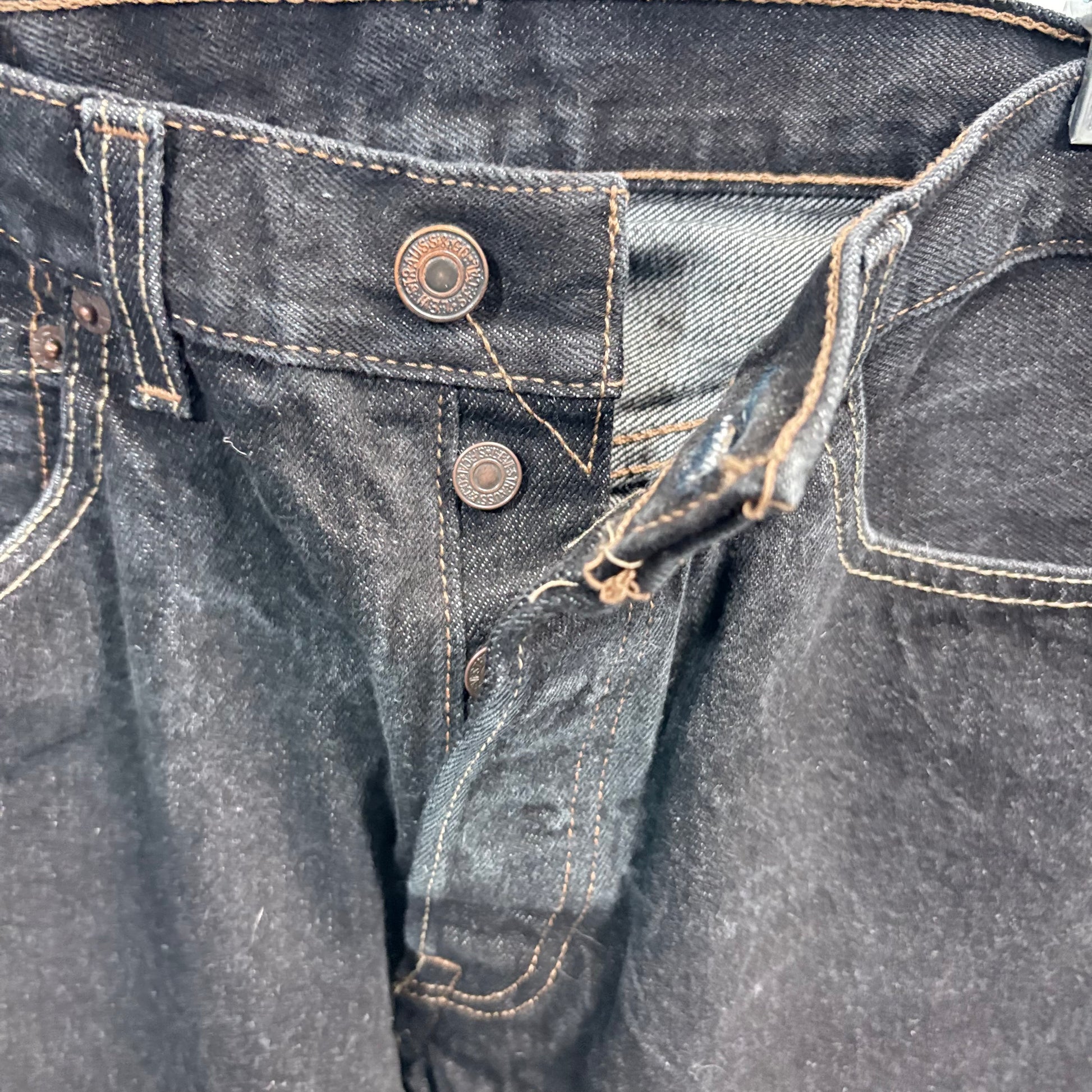 Close-up of dark blue denim jeans with buttons and stitching details.