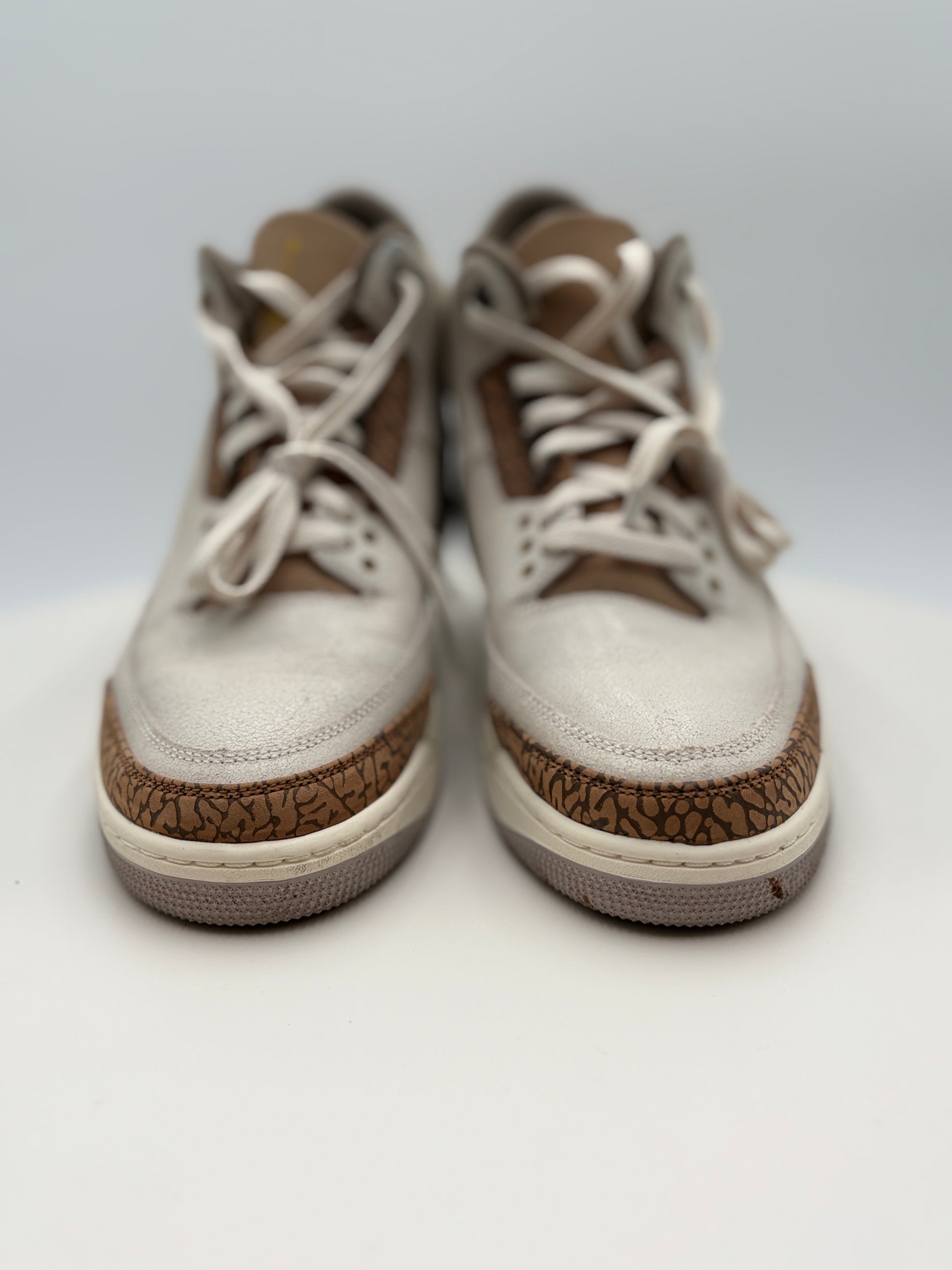 Pair of white sneakers with brown accents on a light gray background