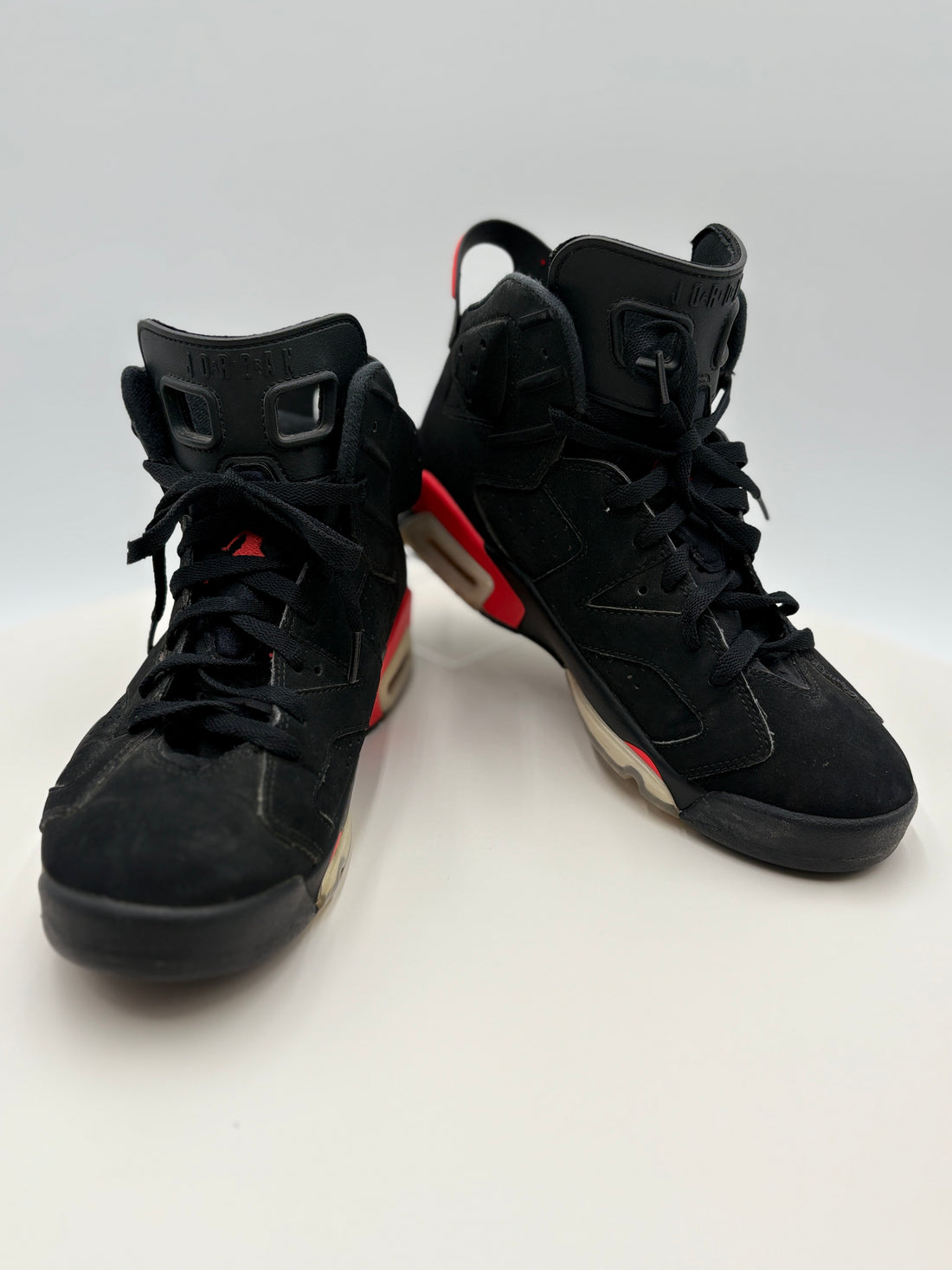 Black high-top sneakers with red accents on a white platform, accompanied by an authenticity certificate.