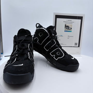 Black high-top sneakers with white accents on a white platform, accompanied by a certificate of authenticity.