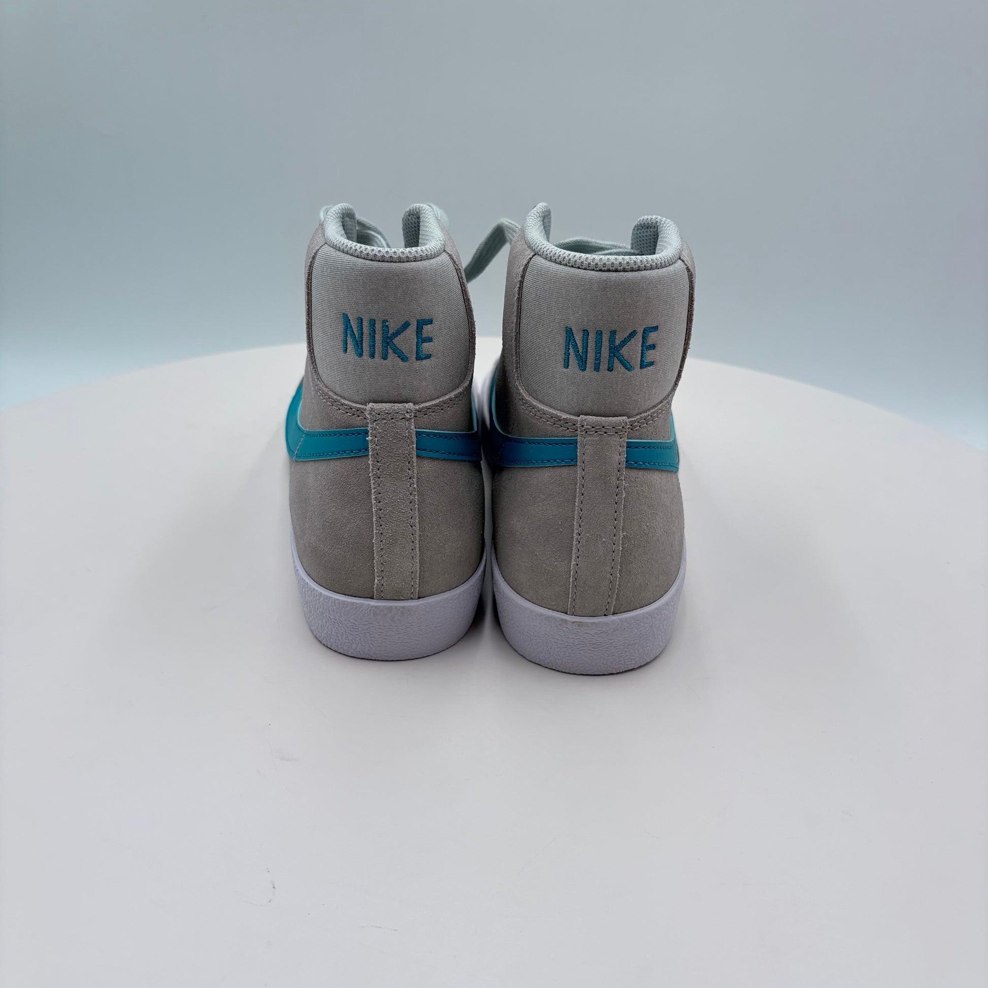 Gray high-top sneakers with blue stripes and 'Nike' branding on a light gray background
