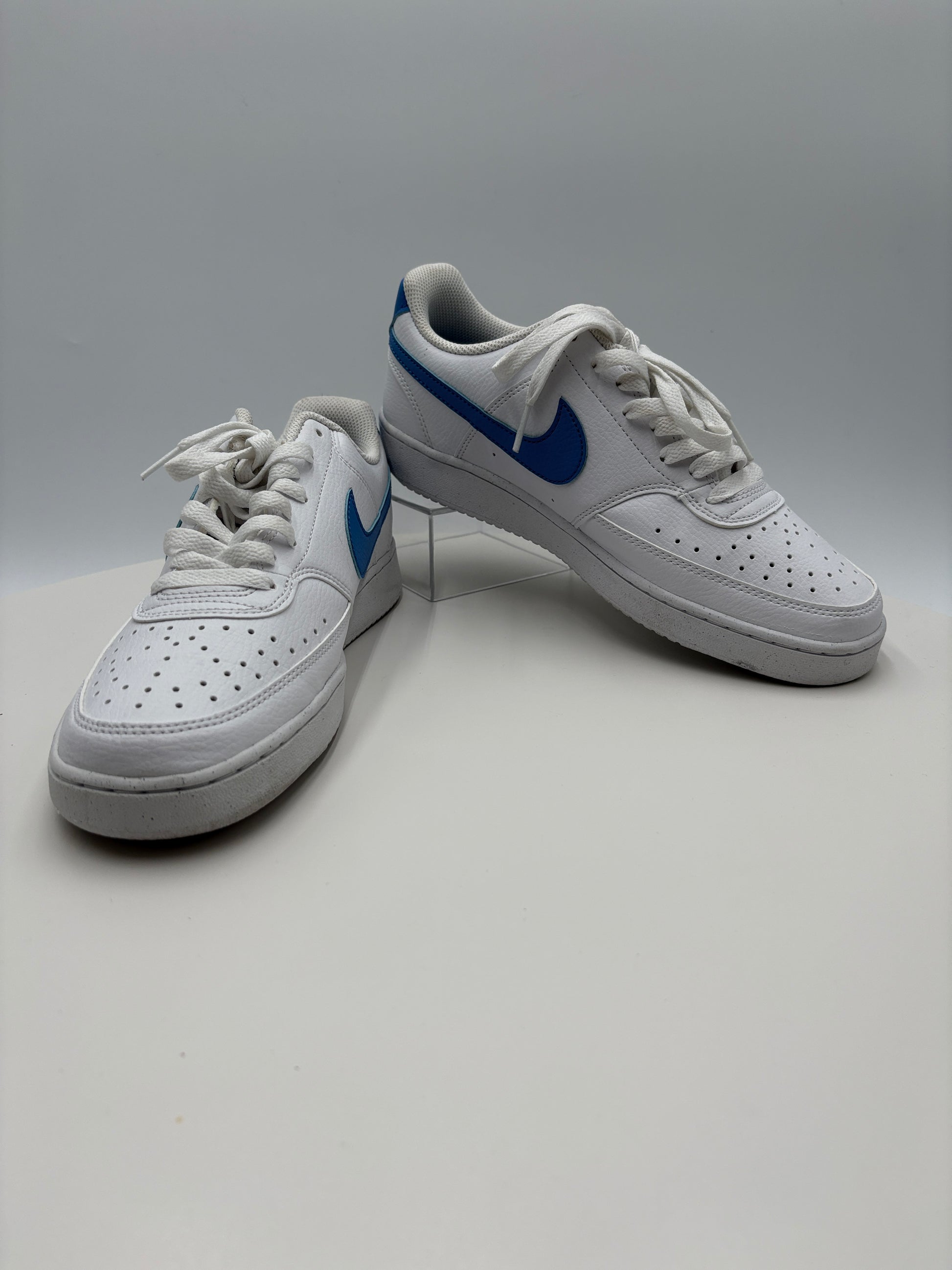 White sneakers with blue accents leaning against a light gray wall.