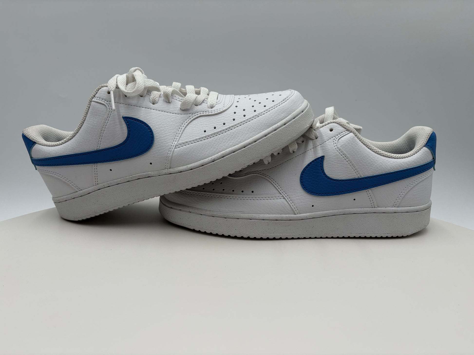 White sneakers with blue swoosh logo on a gray background