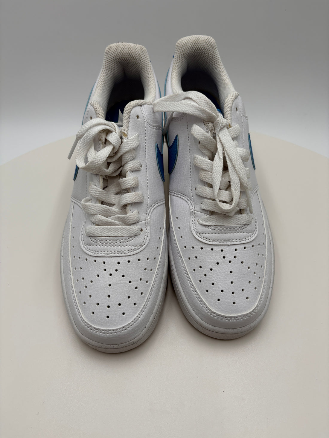 White sneakers with blue accents leaning against a light gray wall.