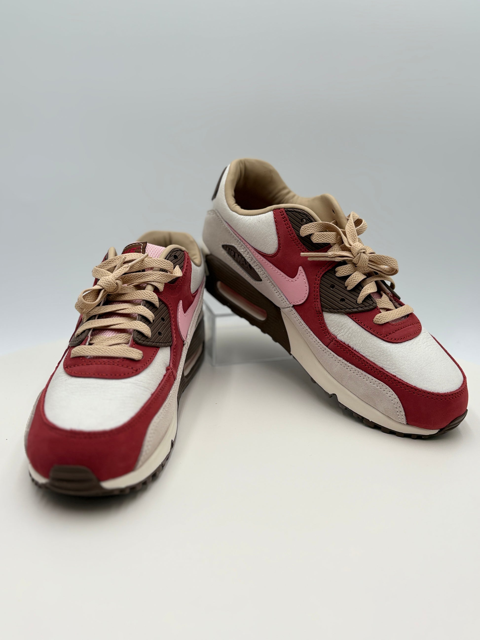 Pair of Nike DQM Air Max 90 Bacon -  red and white sneakers with a Nike logo on a light gray background