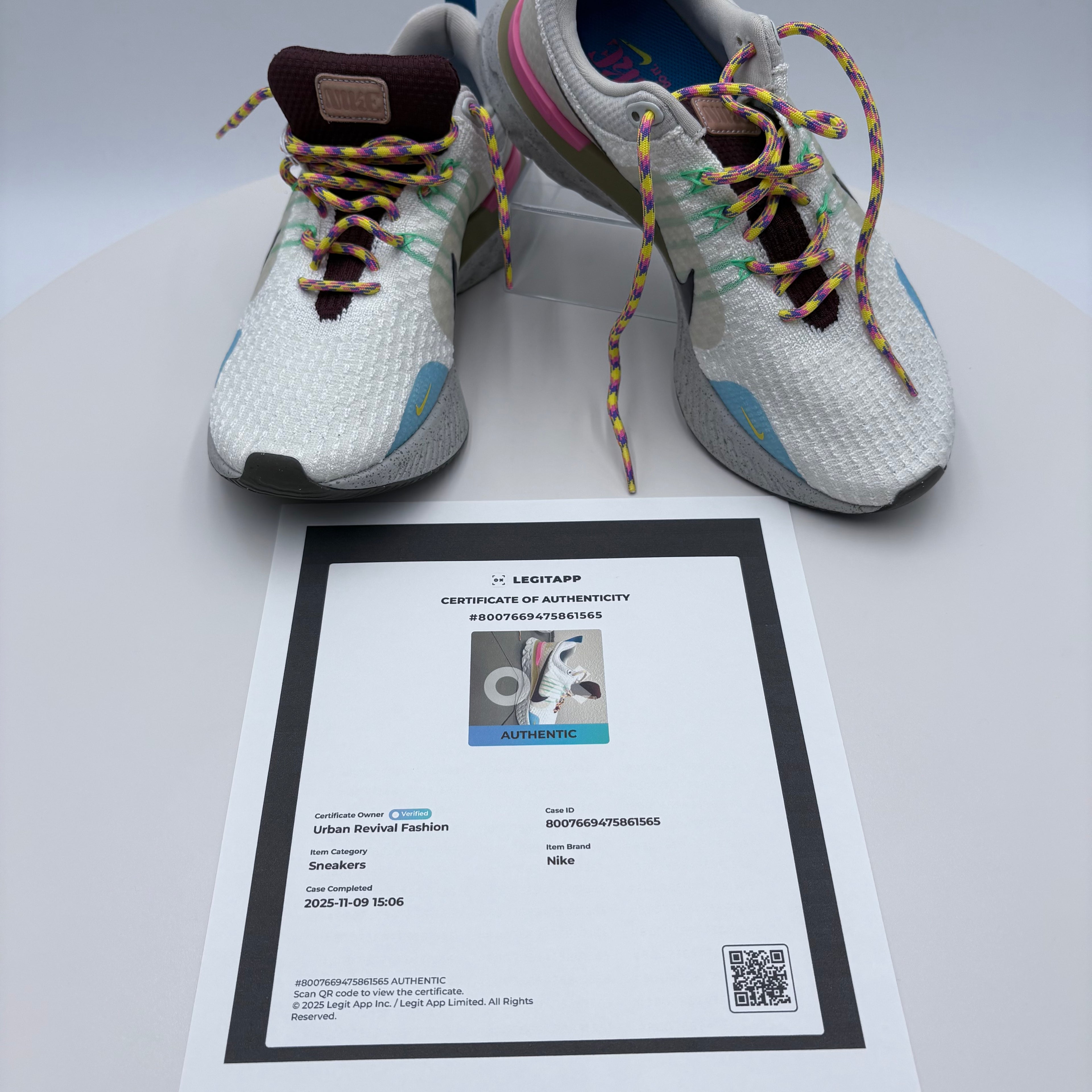 Pair of white sneakers with colorful laces on a white surface, accompanied by a certificate of authenticity.