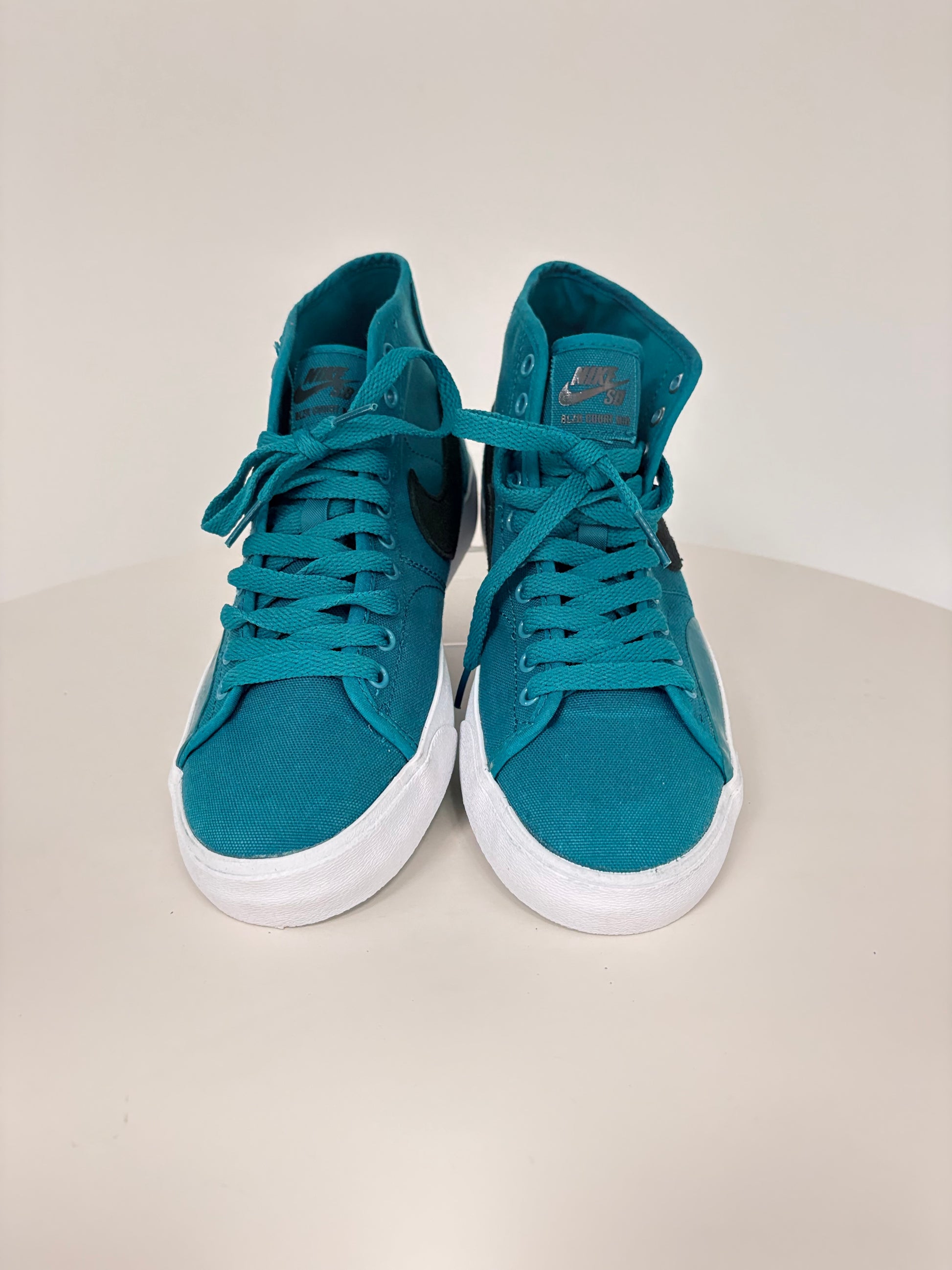 Pair of teal sneakers with white soles on a light beige background