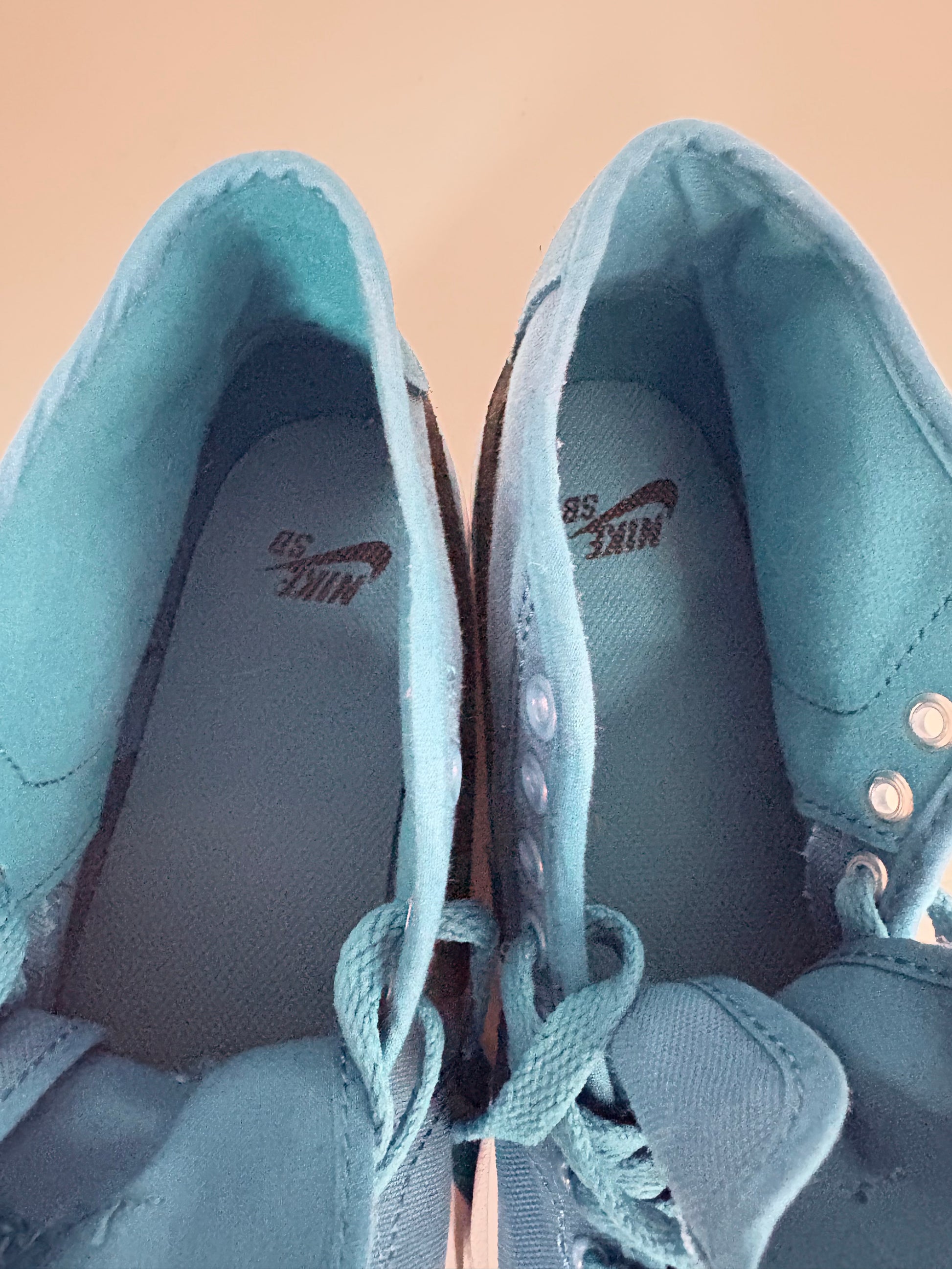 Pair of light blue sneakers with Nike logo on a beige background