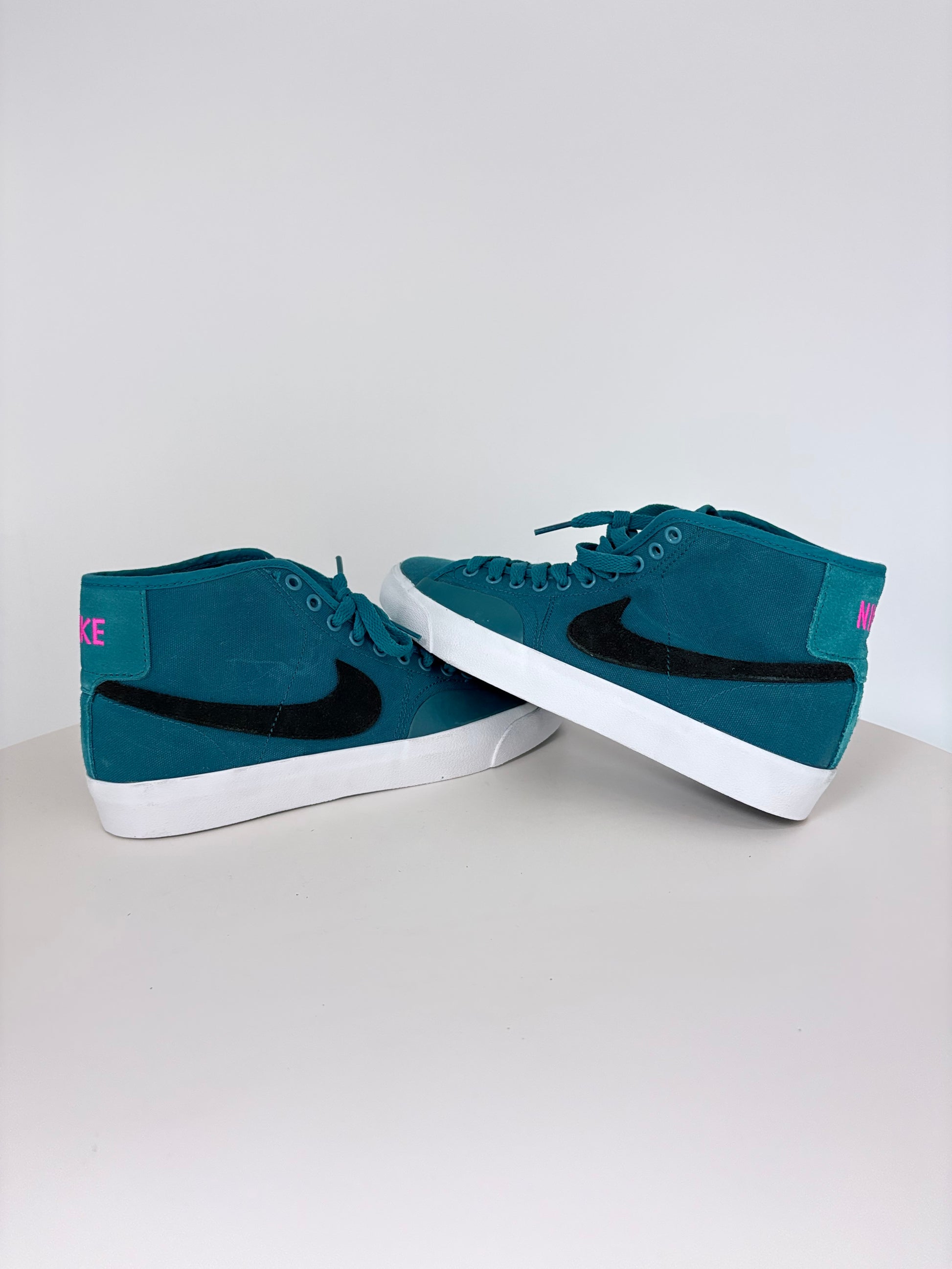Pair of teal sneakers with a black swoosh logo on a light gray background