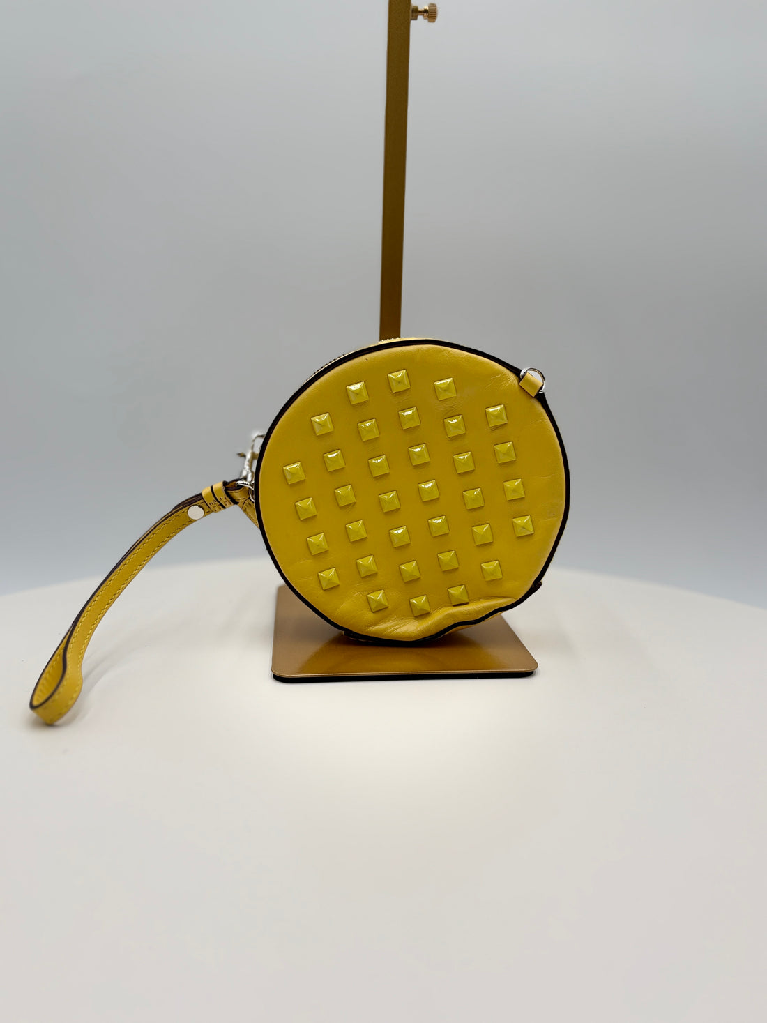 Yellow textured round bag with a strap on a stand against a gray background