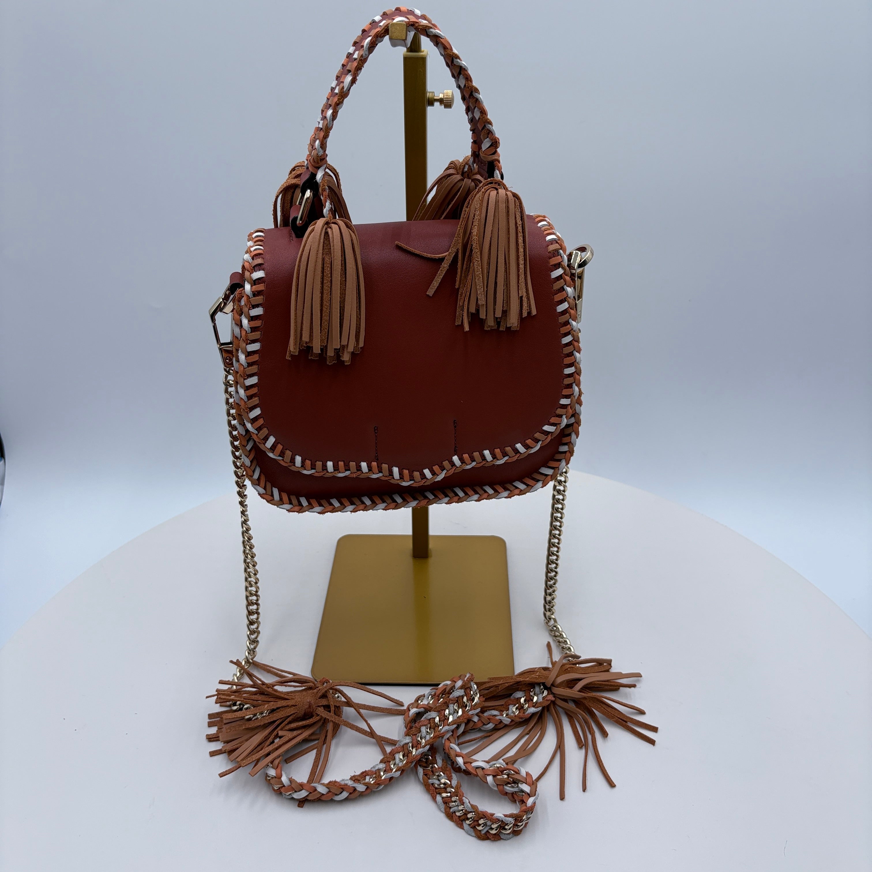 Brown handbag with tassels and leather stitching on a white background