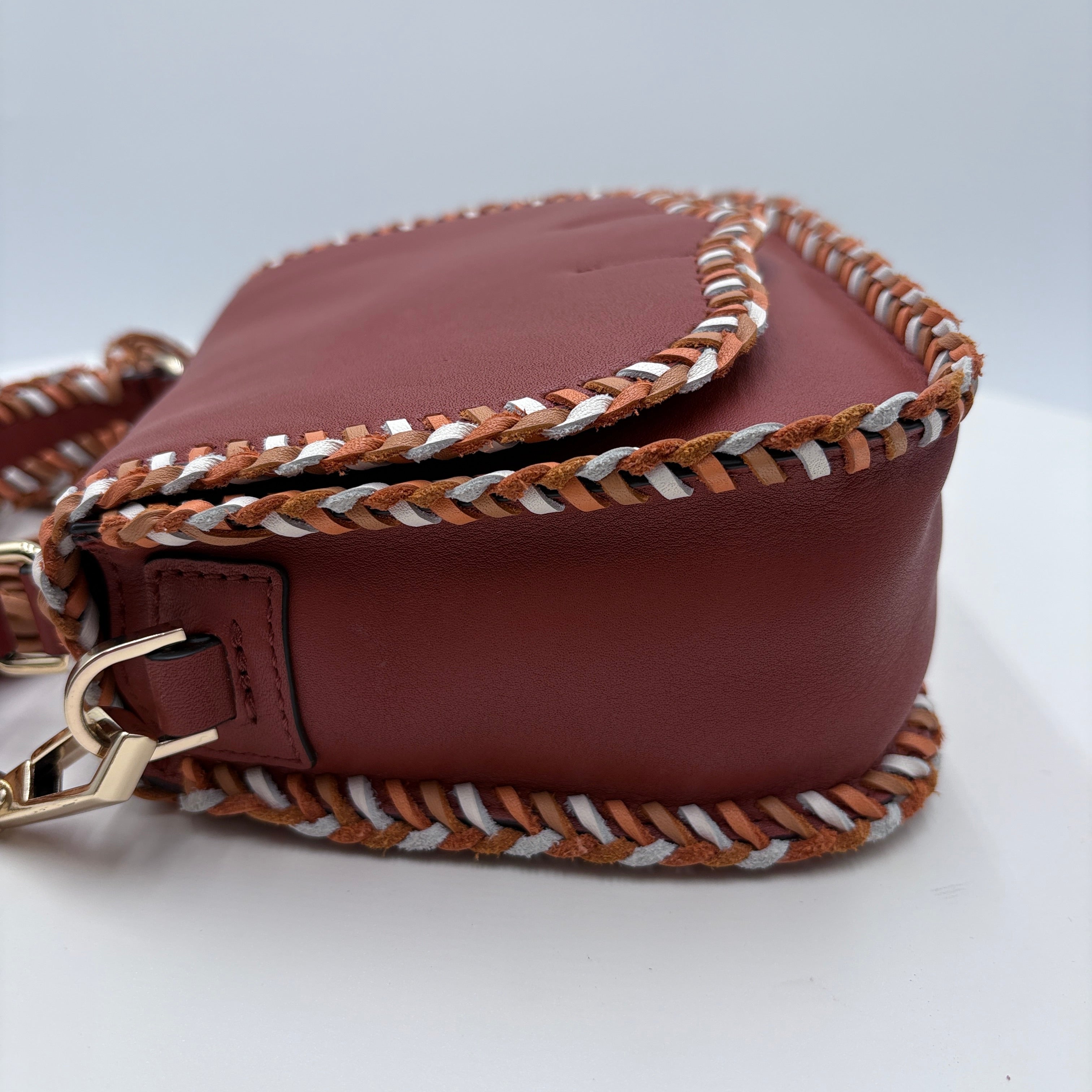 Brown leather handbag with braided handle on a light gray background