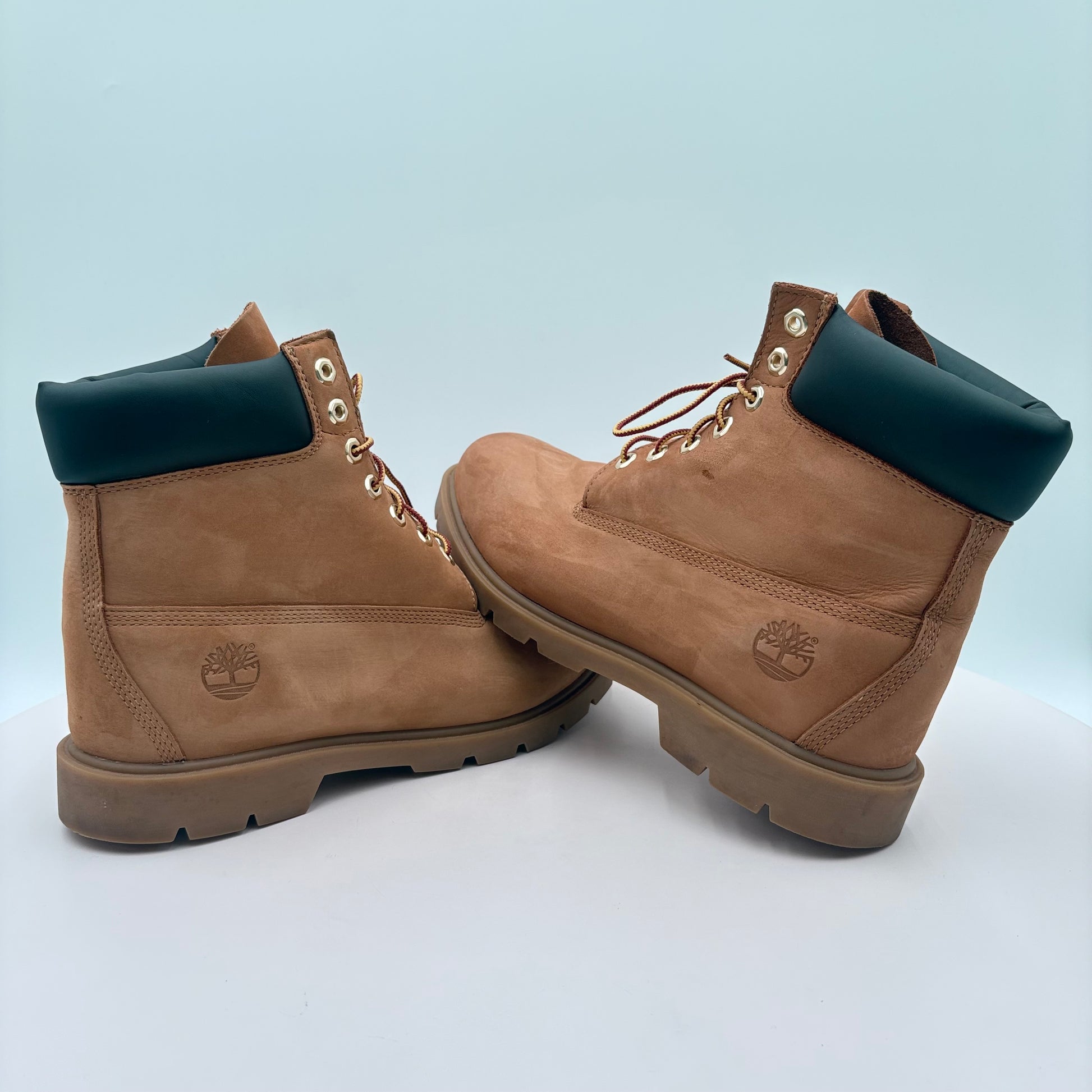 Pair of brown Timberland boots with black collars on a light blue background