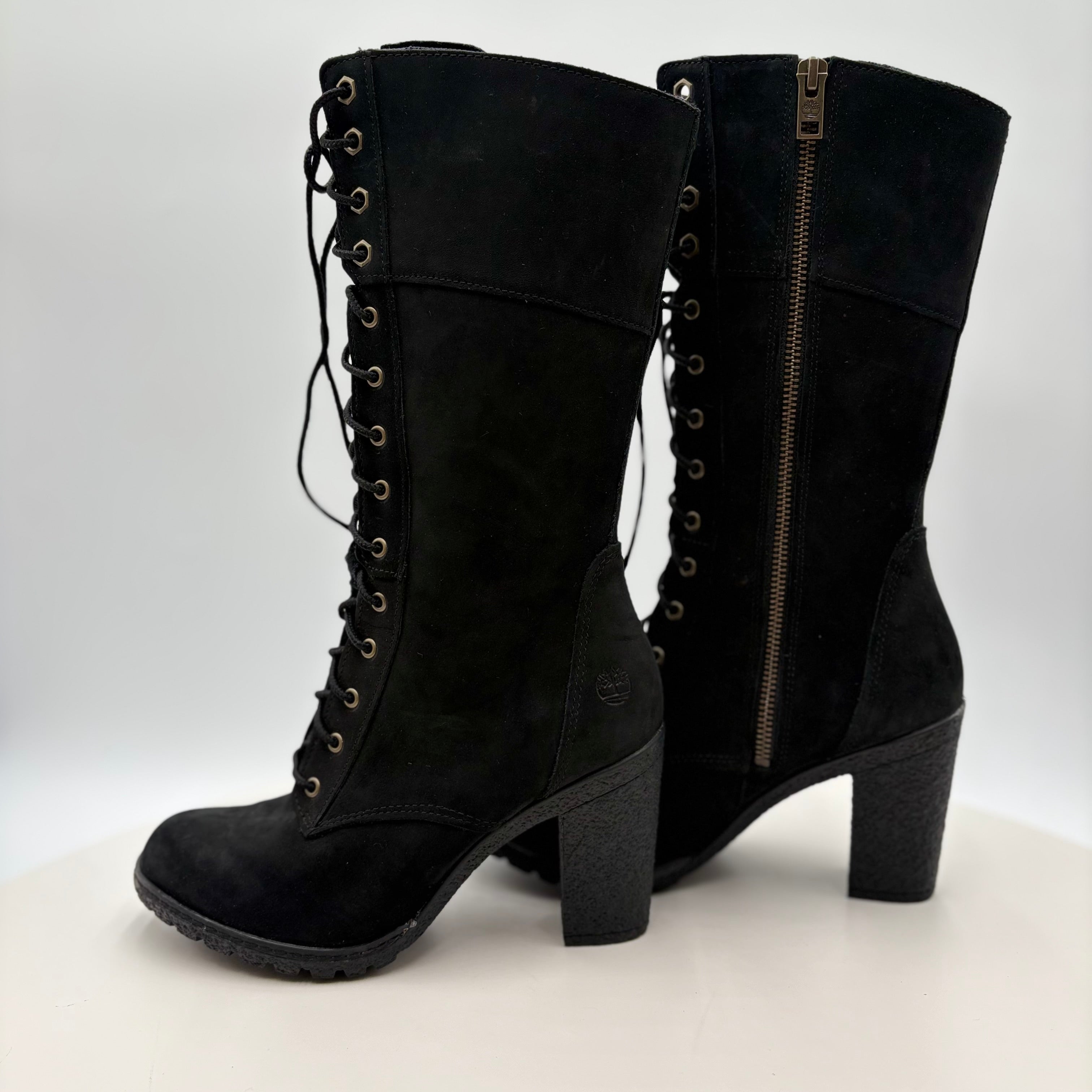Black suede knee-high boots with lace-up design and zipper on a white background