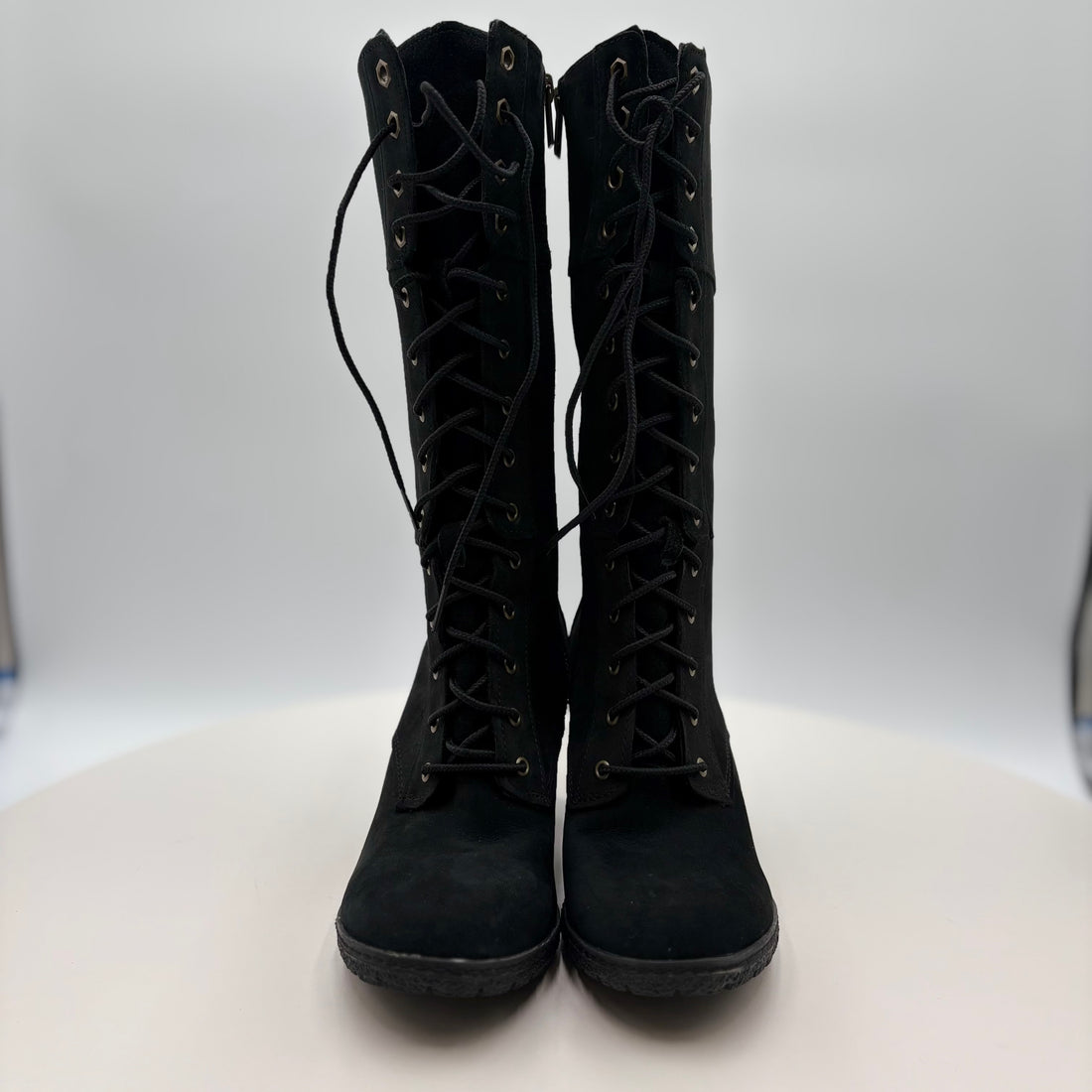 Pair of black knee-high boots with laces and a zipper on a white background